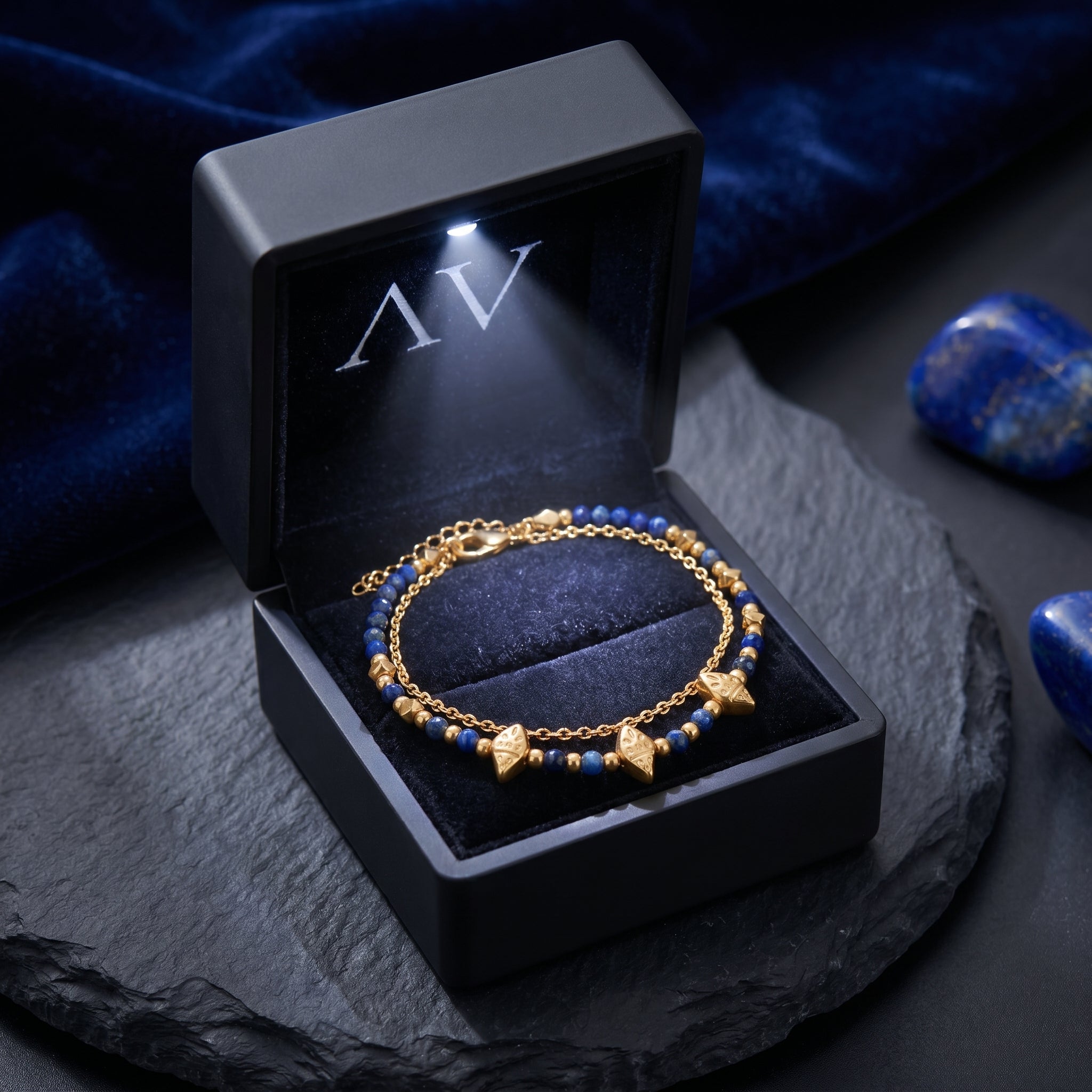18k gold-plated lapis bead bracelet presented in a black LED-lit jewelry gift box on a stone surface.
