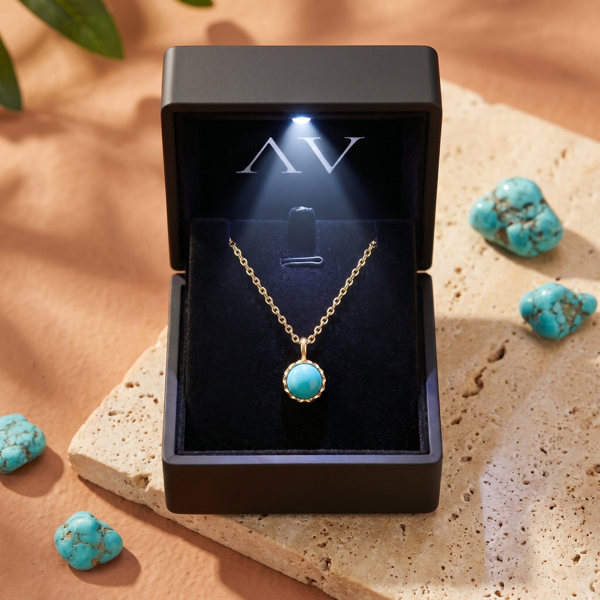 Gold vermeil turquoise necklace presented in a black lighted gift box, surrounded by raw turquoise stones on a stone slab.