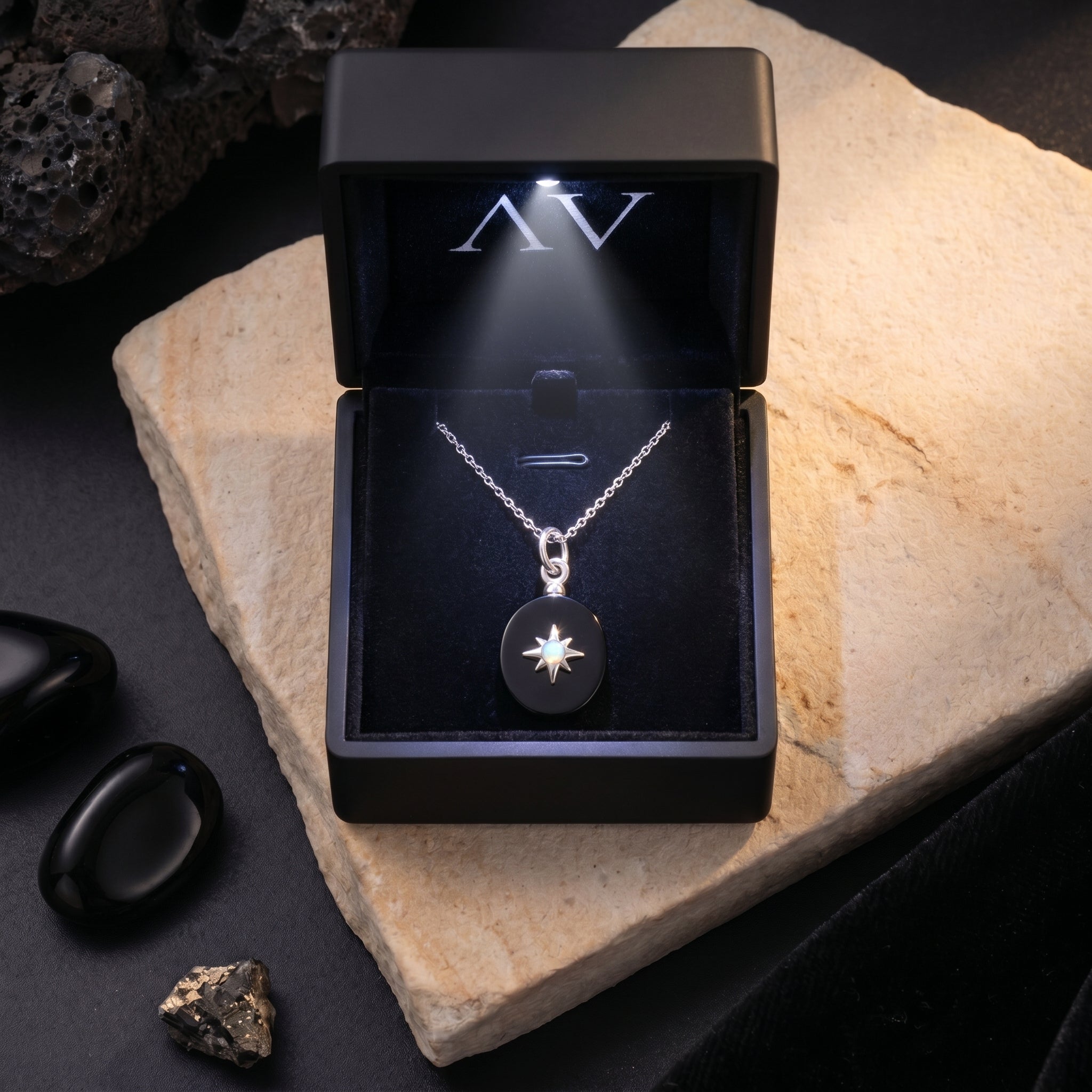 Oval black onyx pendant necklace presented in a black LED-lit jewelry gift box on a stone surface.