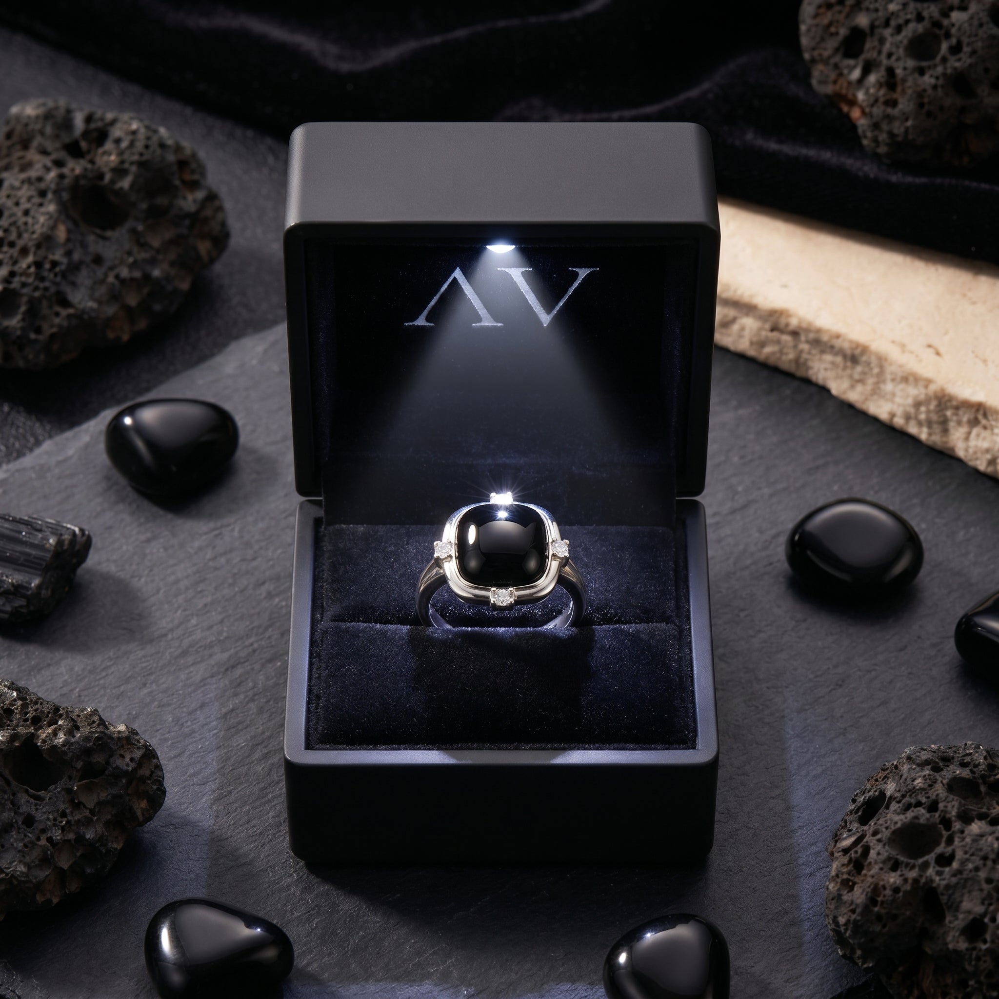 Natural black onyx cushion ring in a premium black LED-lit presentation box surrounded by volcanic stones.