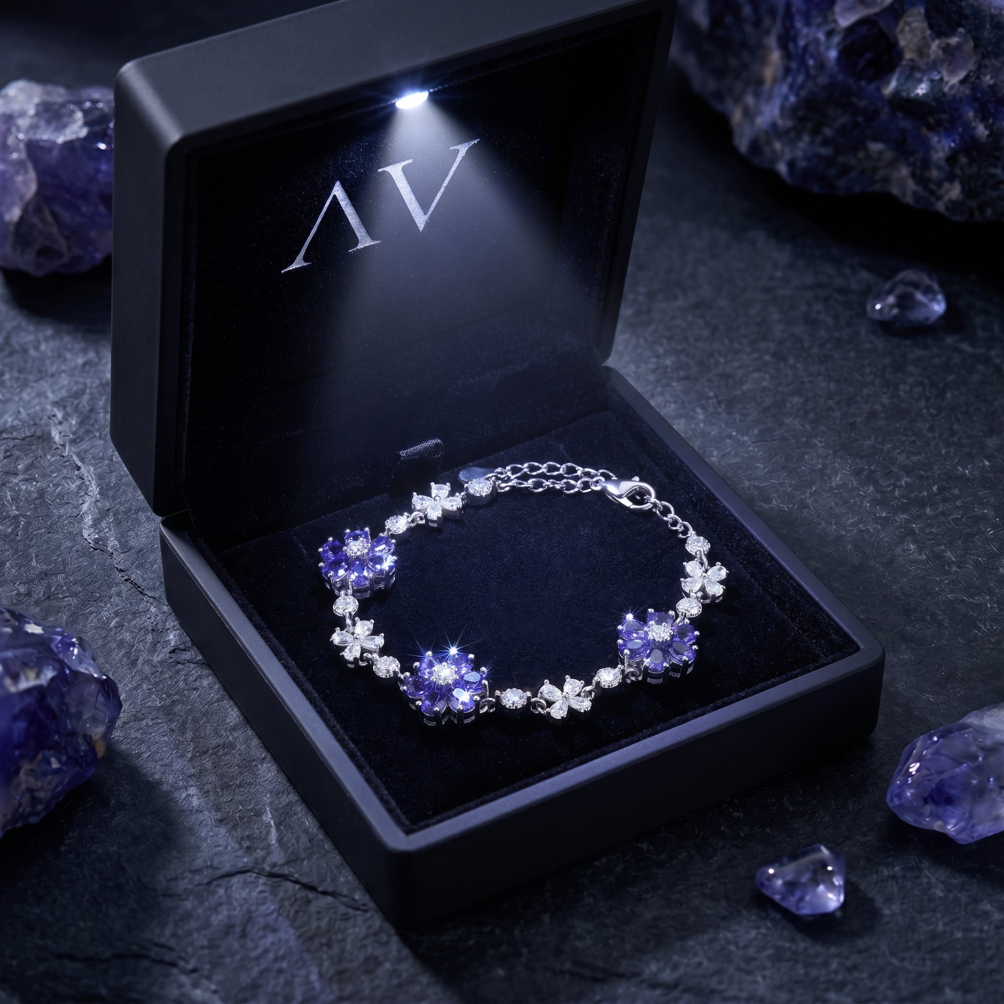 Sterling silver tanzanite cluster bracelet presented in a black light-up gift box on a stone surface.