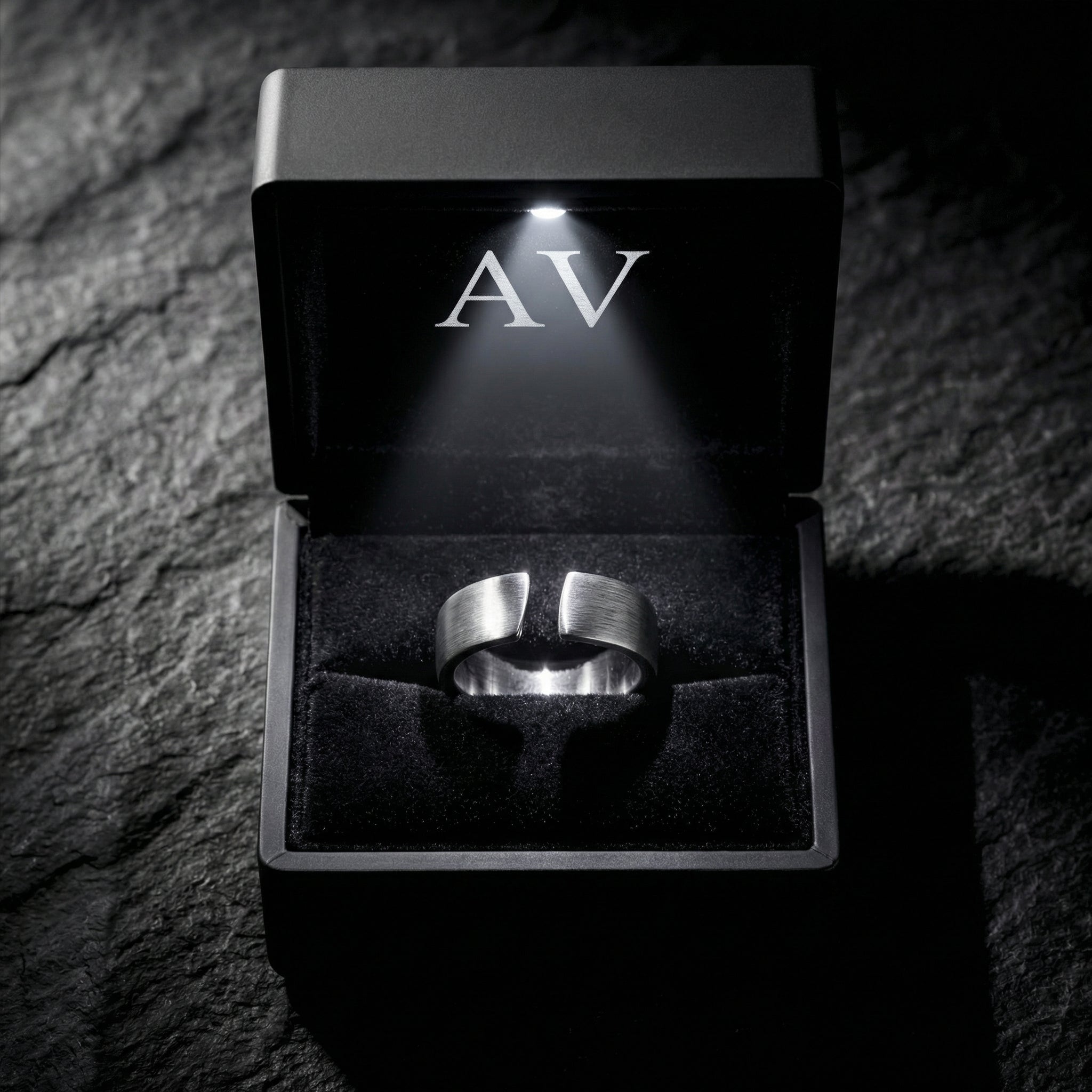 Brushed silver stainless steel Spartan band ring inside a black LED-lit gift box on a stone background.