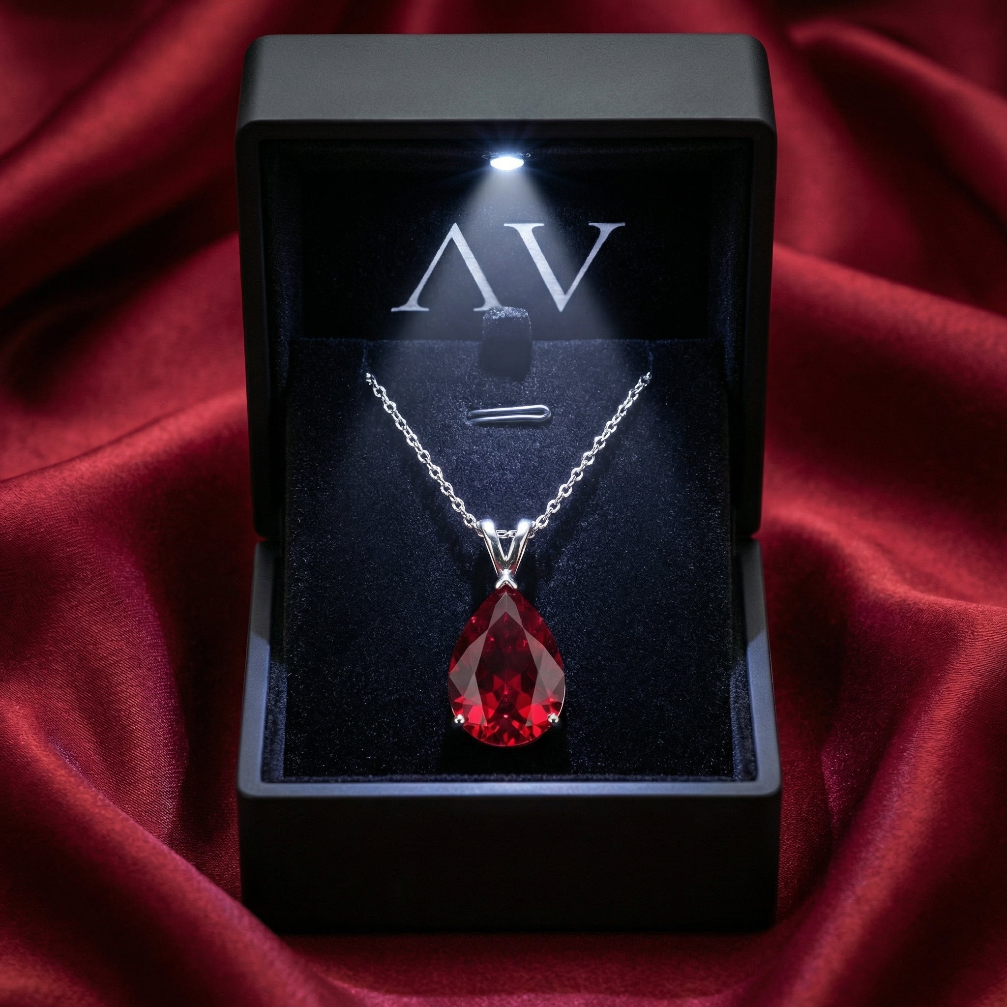 Pear cut red moissanite necklace in a lighted black gift box on red satin background.
