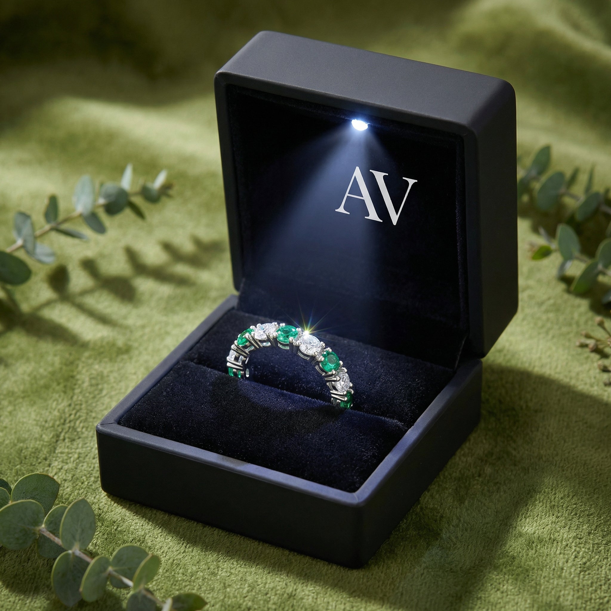S925 silver simulated emerald eternity ring in a black LED-lit jewelry box on a green textured background.