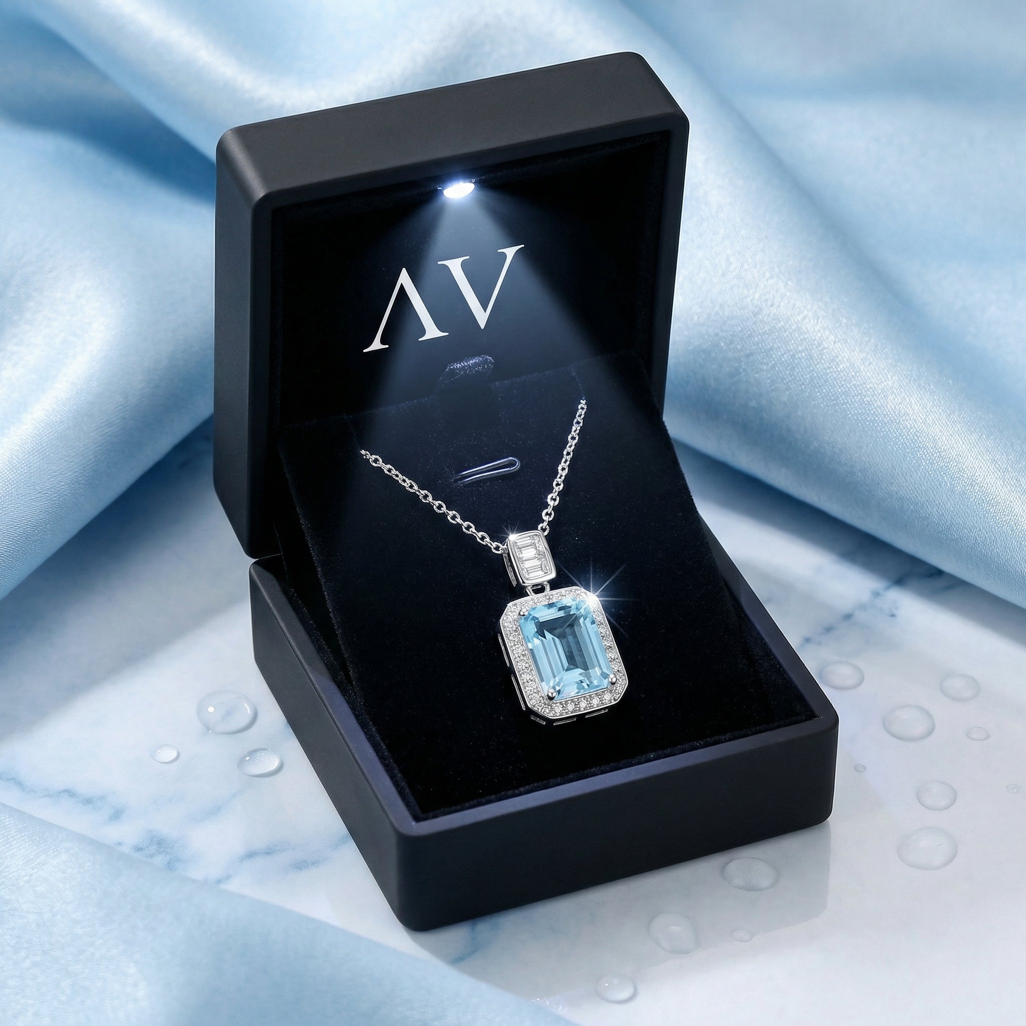 Emerald-cut simulated aquamarine pendant inside a lighted black jewelry gift box on blue silk.