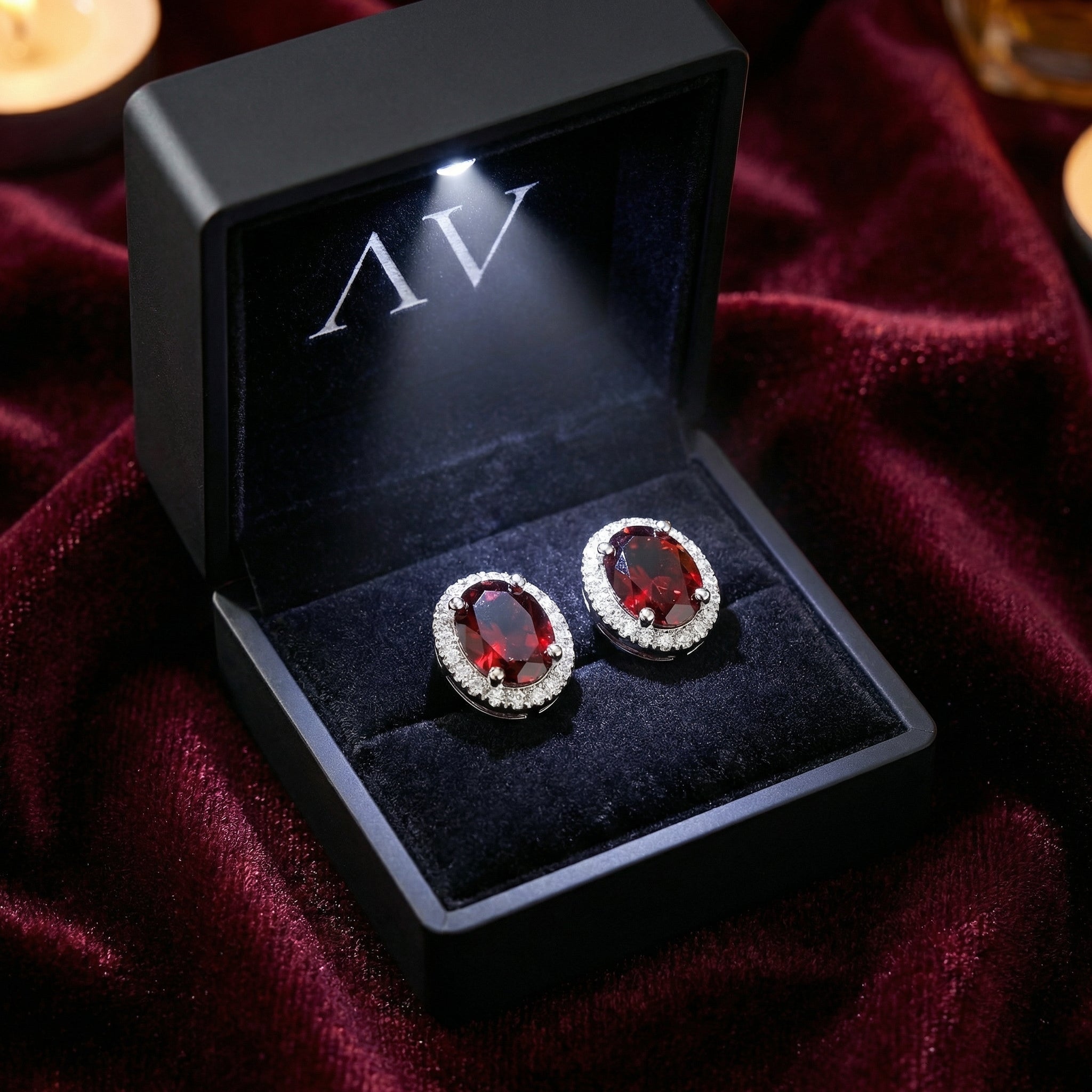 Oval simulated garnet halo stud earrings in sterling silver presented in a black LED-lighted gift box.