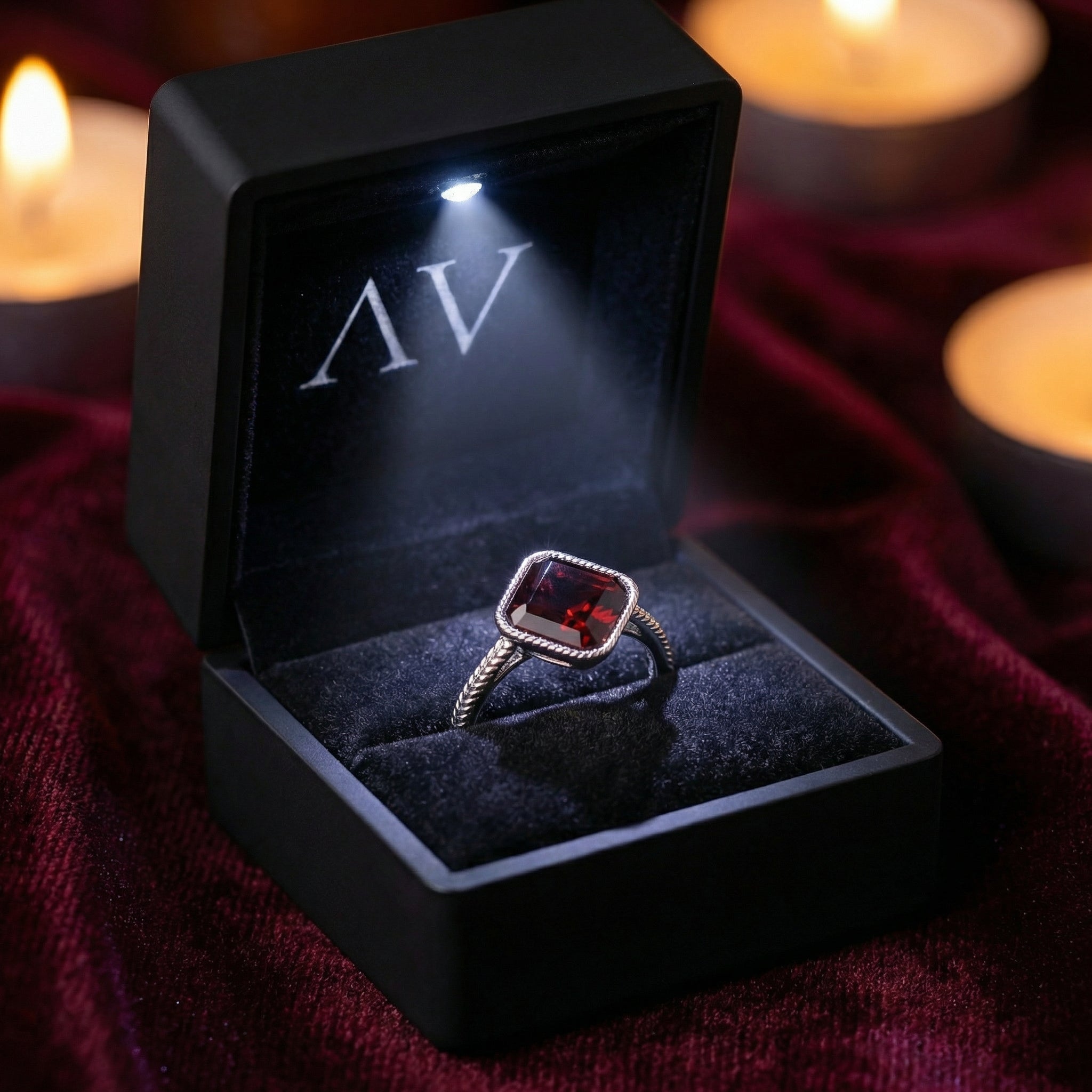 Sterling silver cushion-cut simulated garnet ring in a black LED-lit jewelry box on red velvet.