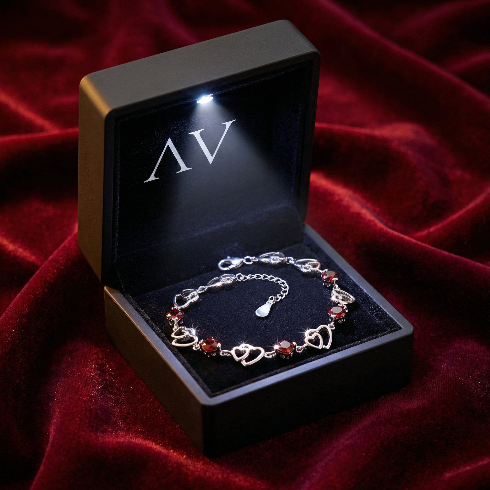 Sterling silver heart bracelet with simulated garnets inside a black LED-lit jewelry gift box on red velvet.