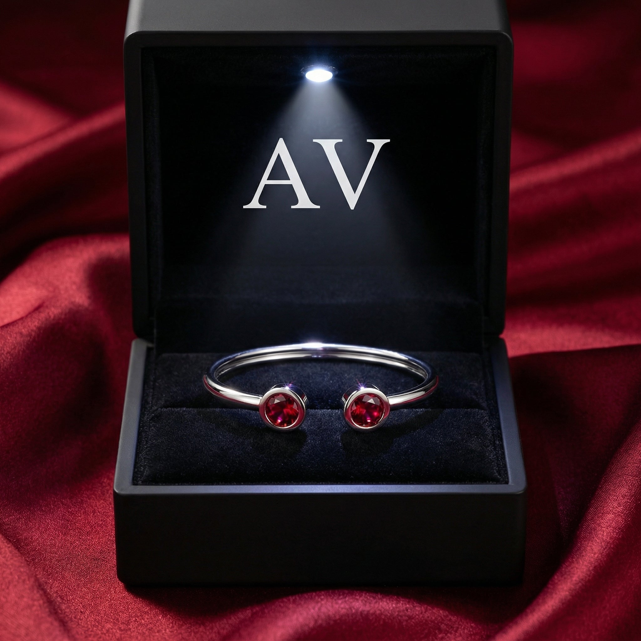 Silver stainless steel Selenis bangle with red rubies presented in a black LED-lit jewelry gift box.