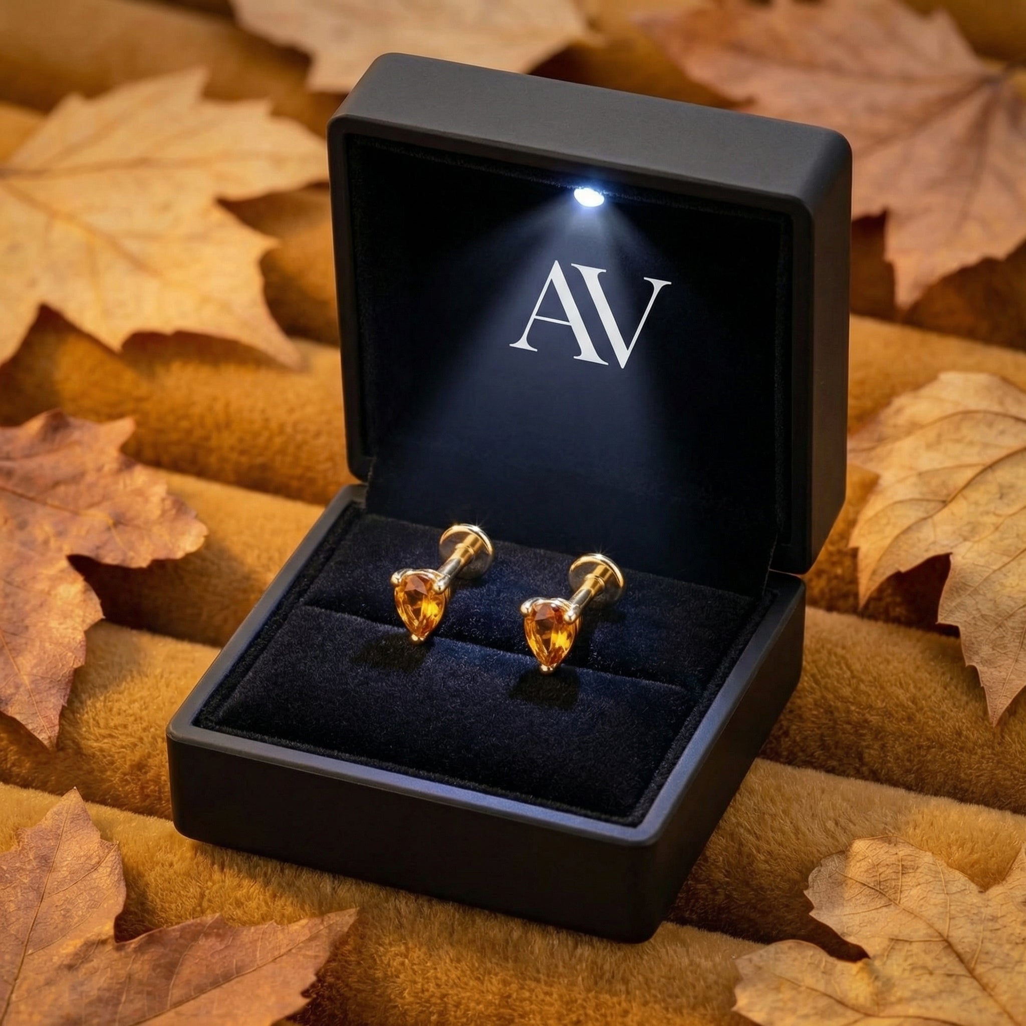 Pear-cut simulated topaz gold vermeil earrings in a black LED-lit gift box surrounded by autumn leaves.