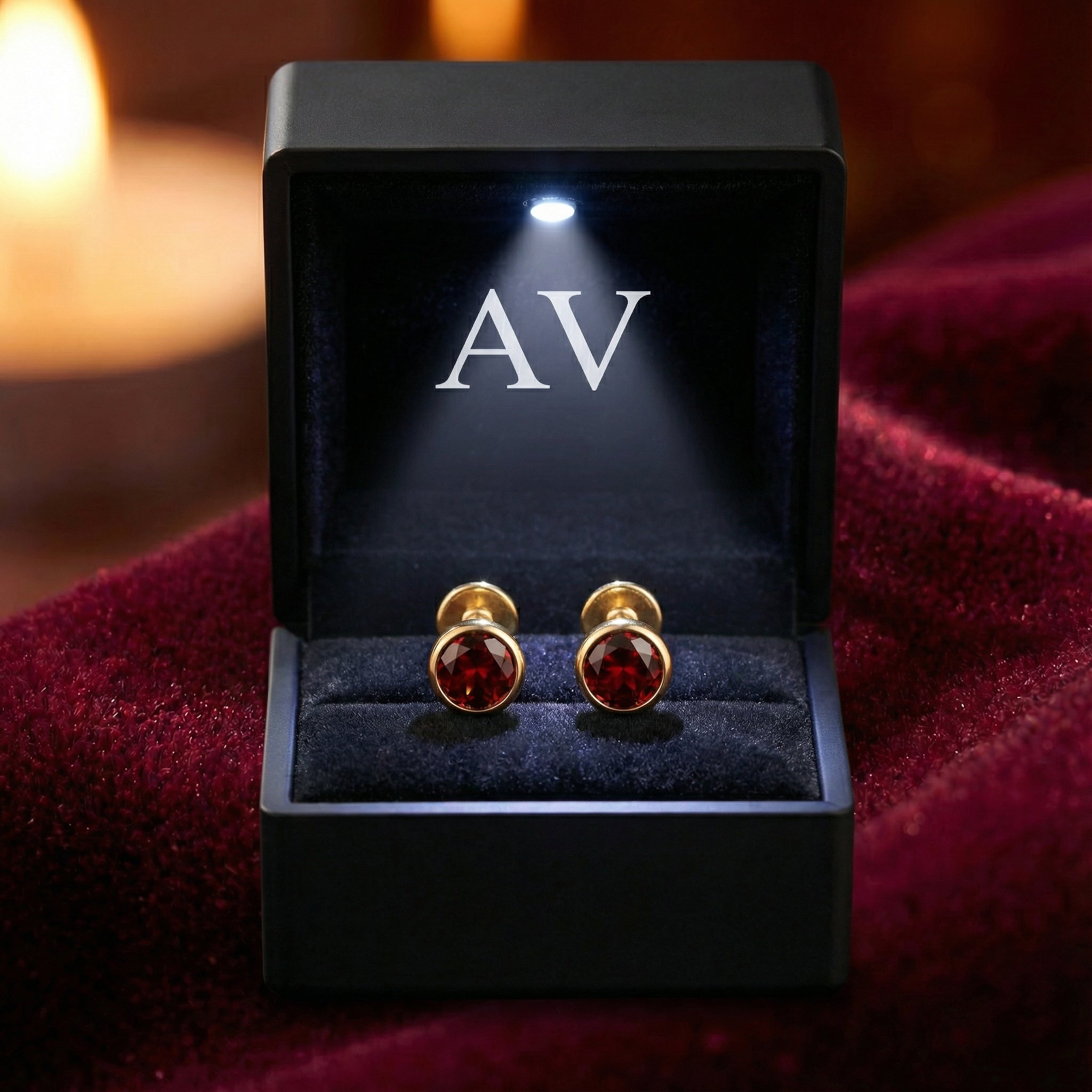 Red simulated garnet stud earrings in 18K gold vermeil inside a lighted black jewelry box on velvet.