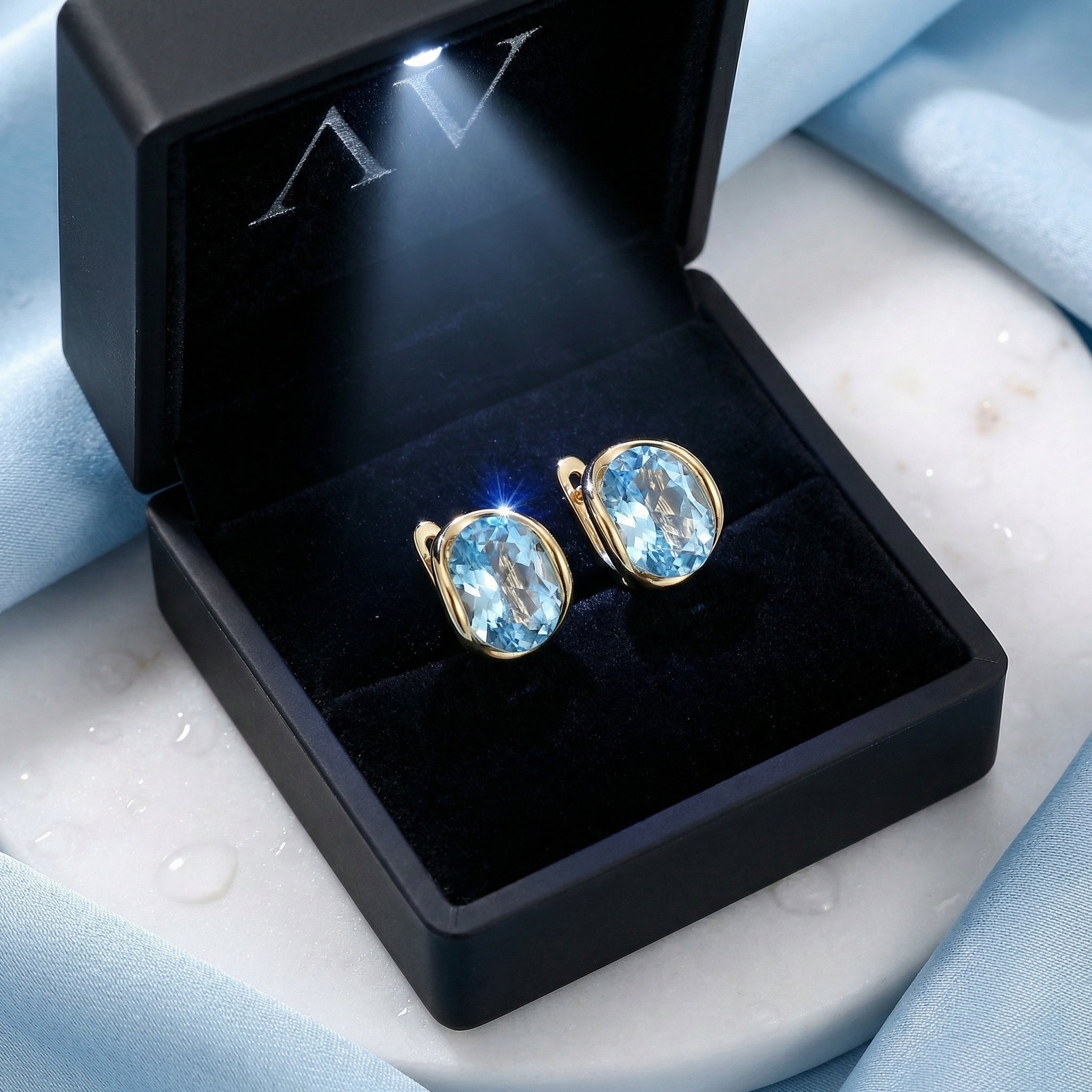 18K gold vermeil huggie earrings with oval simulated aquamarine stones inside a black LED-lit jewelry gift box.