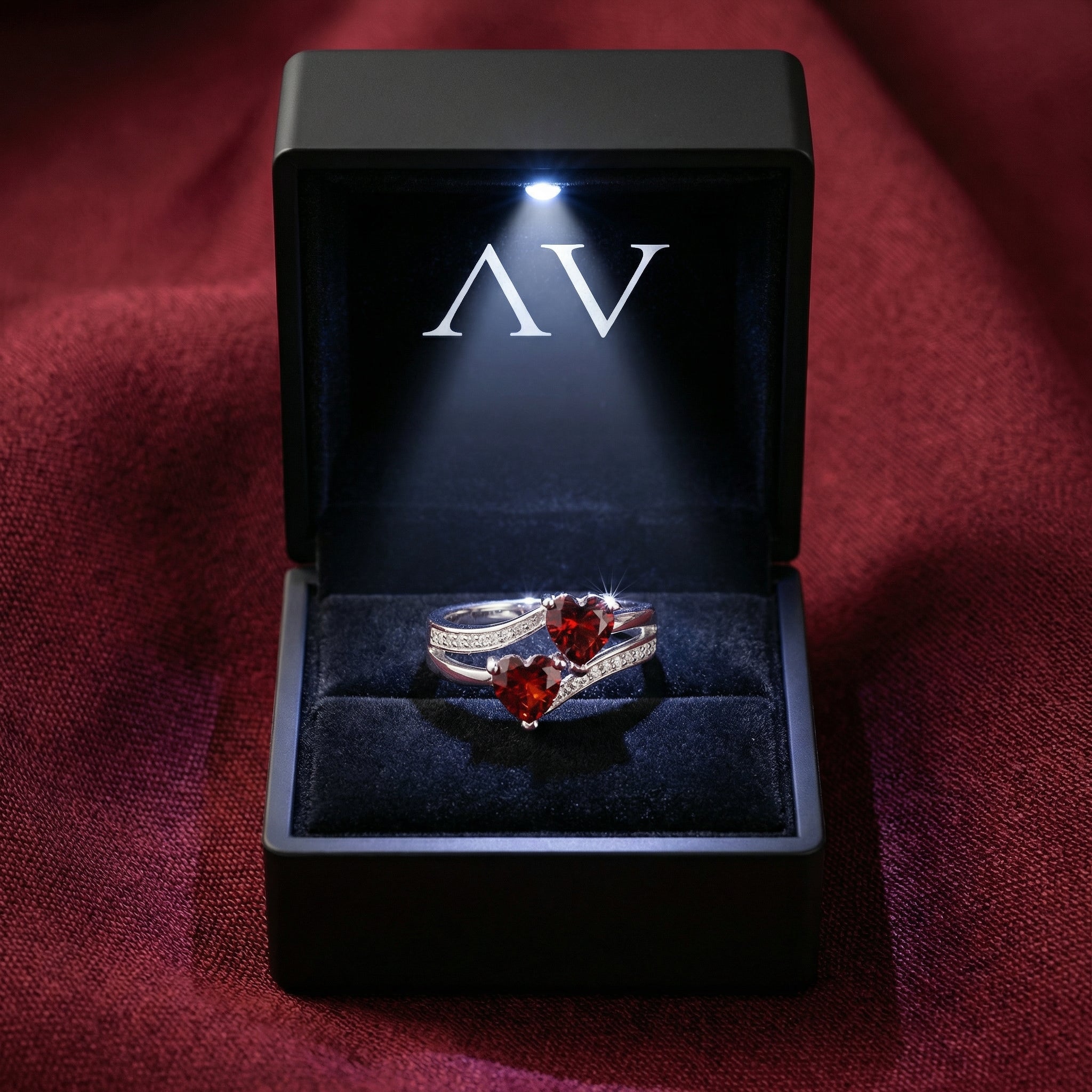 Sterling silver ring with two heart cut simulated garnets inside a black lighted jewelry presentation box.