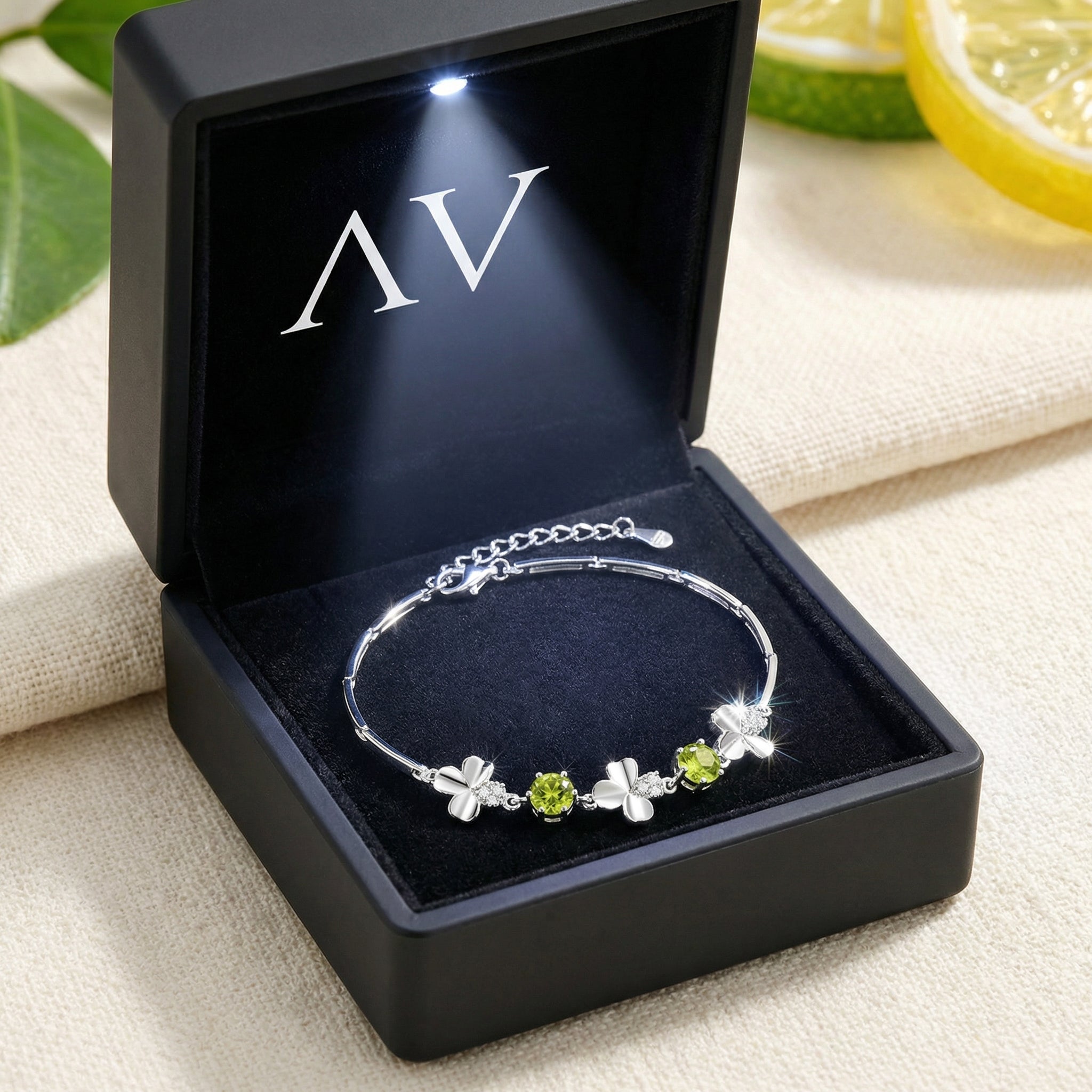Sterling silver clover bracelet with peridot stones displayed in a black LED-lit jewelry presentation box.