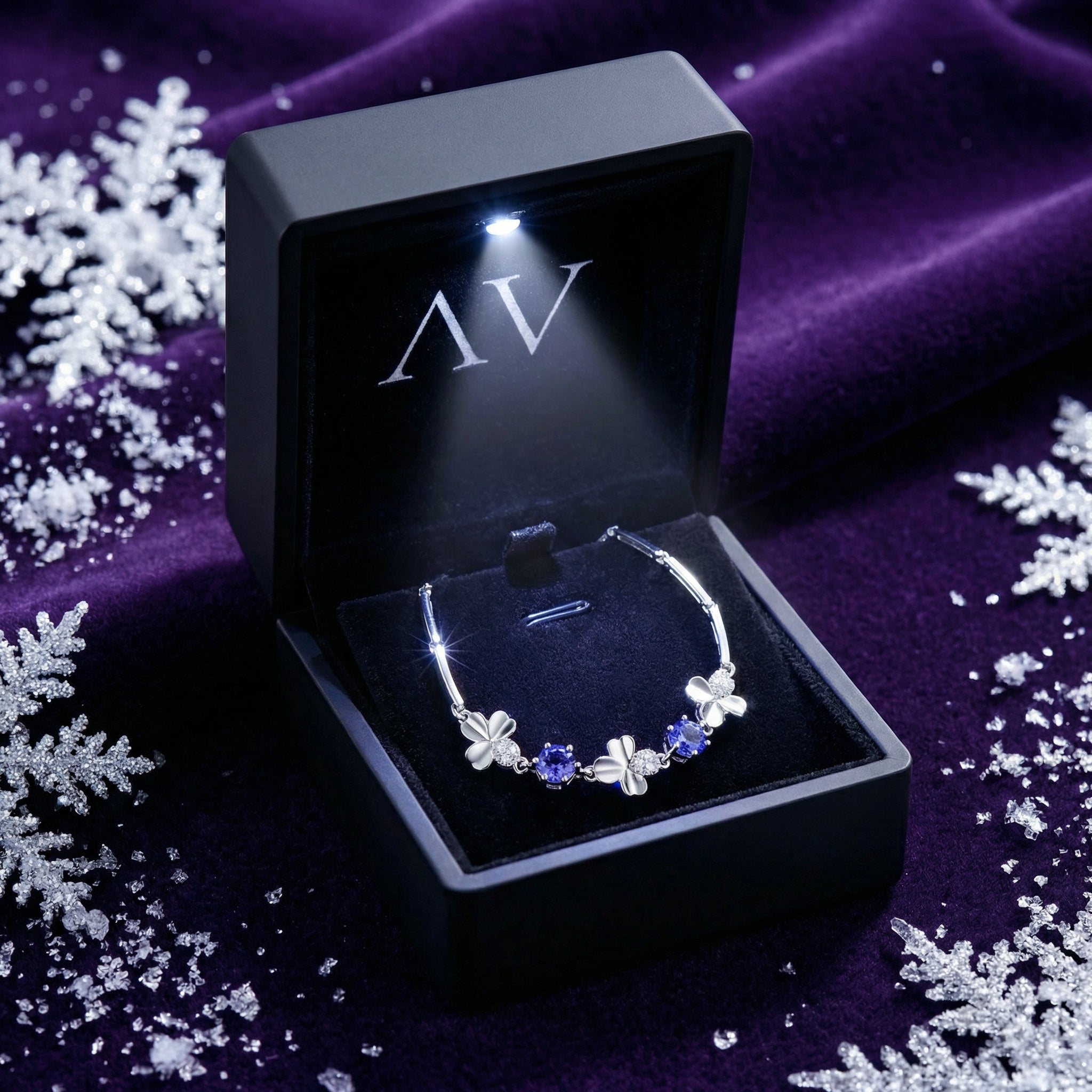 Silver clover bracelet with blue simulated tanzanite stones inside a black LED-lit jewelry gift box.