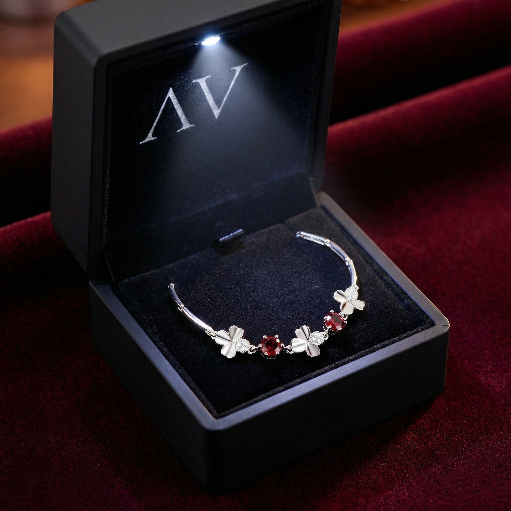 Sterling silver clover bracelet with red simulated garnets inside a black LED-lit jewelry gift box.