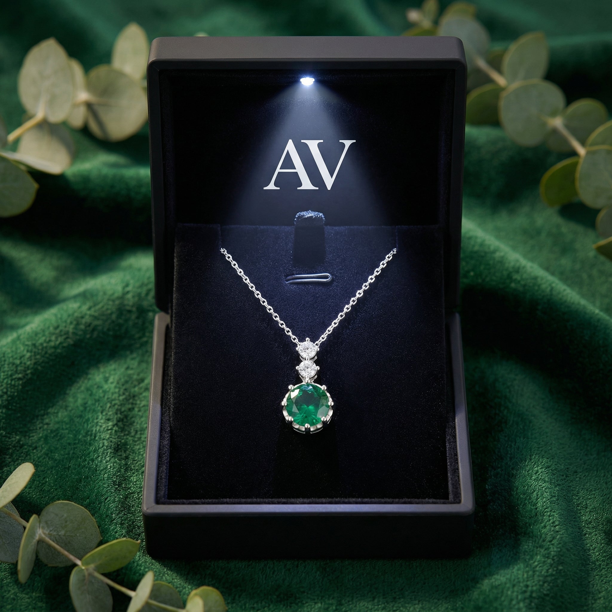 Simulated emerald necklace presented in a black LED-lit gift box on a green velvet background.
