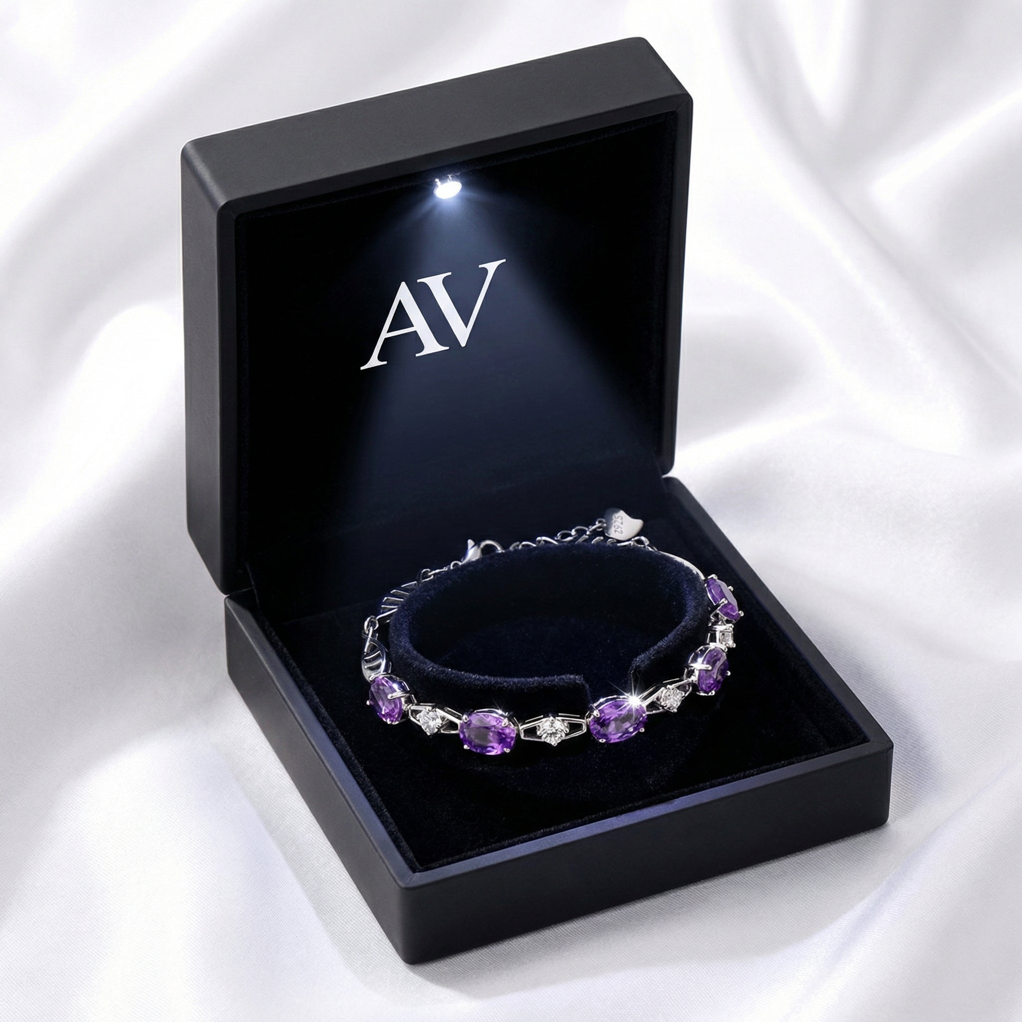 Oval-cut simulated amethyst bracelet displayed on a black cushion inside a lighted premium jewelry box.
