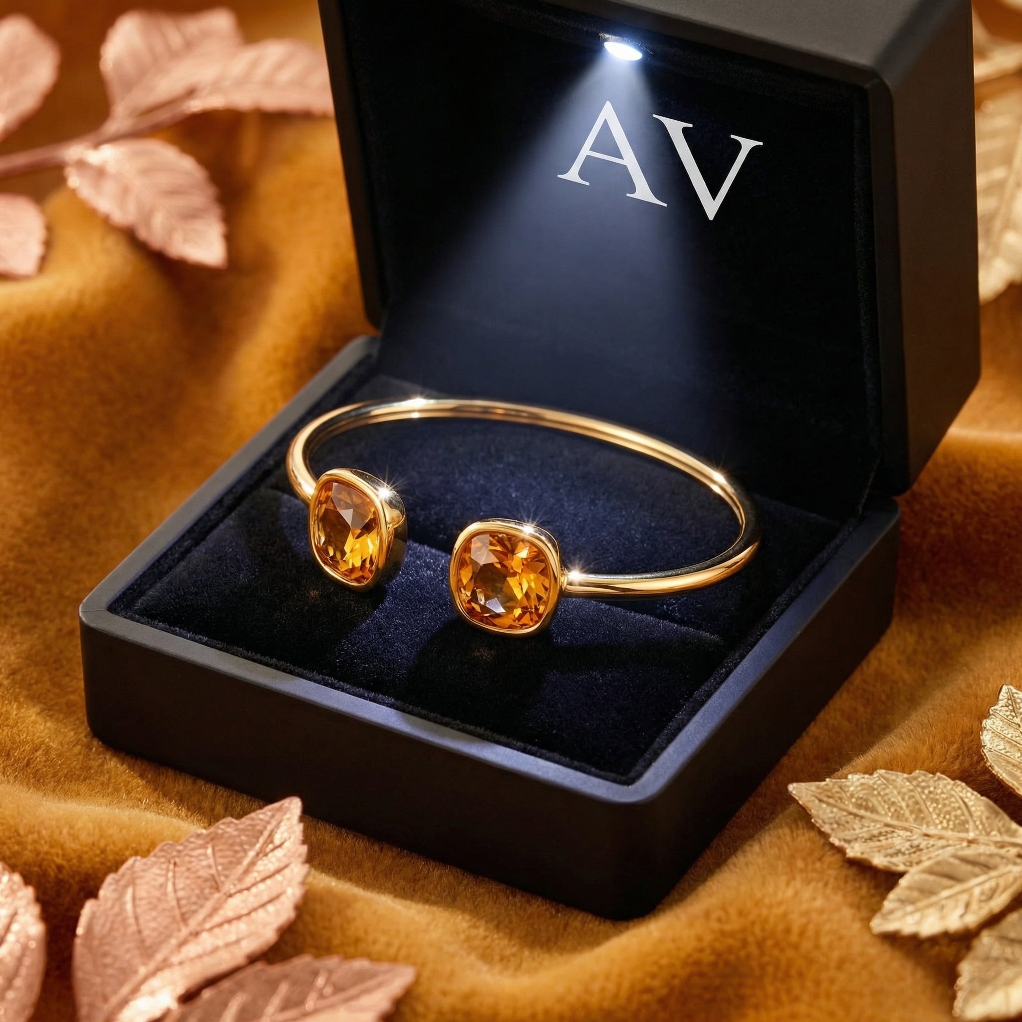Gold-tone stainless steel Hesperian bangle with simulated topaz stones in a lighted black AV jewelry presentation box.