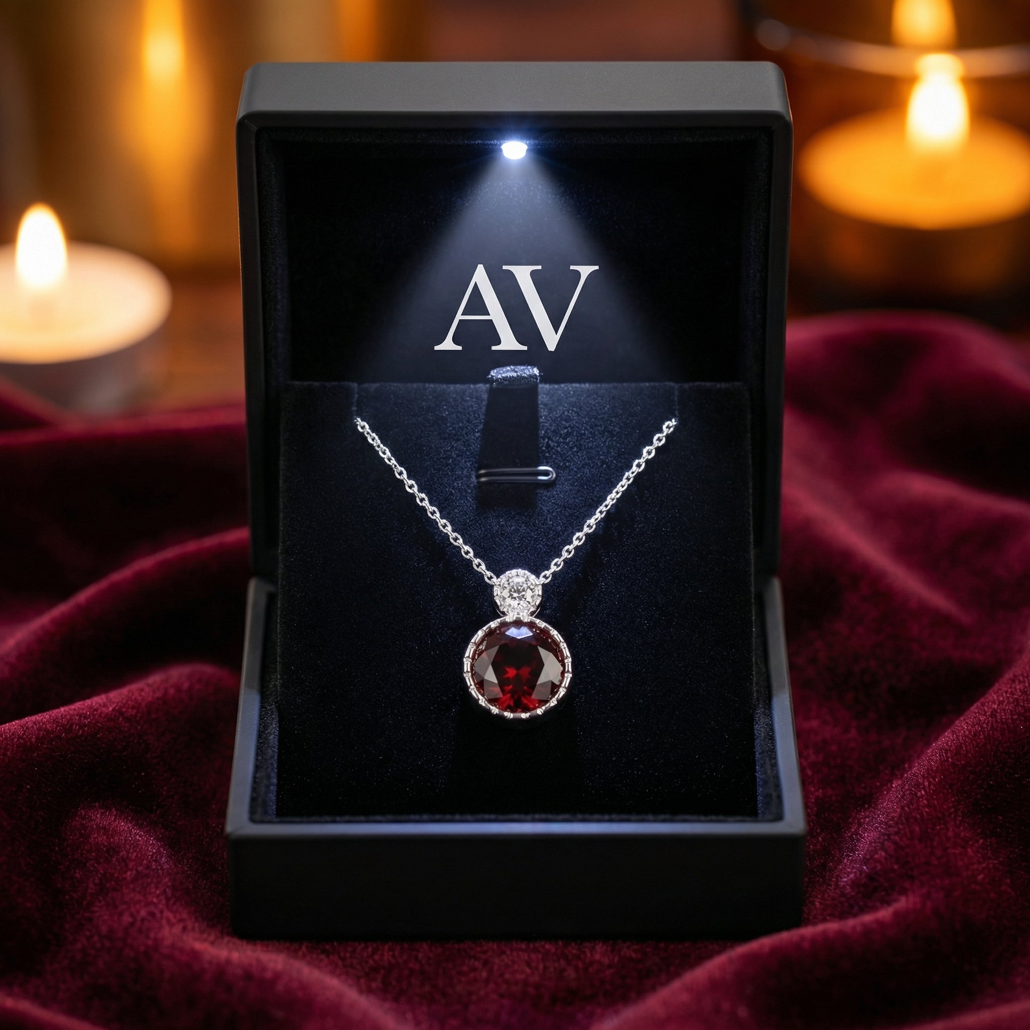 Red garnet sterling silver necklace displayed in a lighted black jewelry box on red velvet.