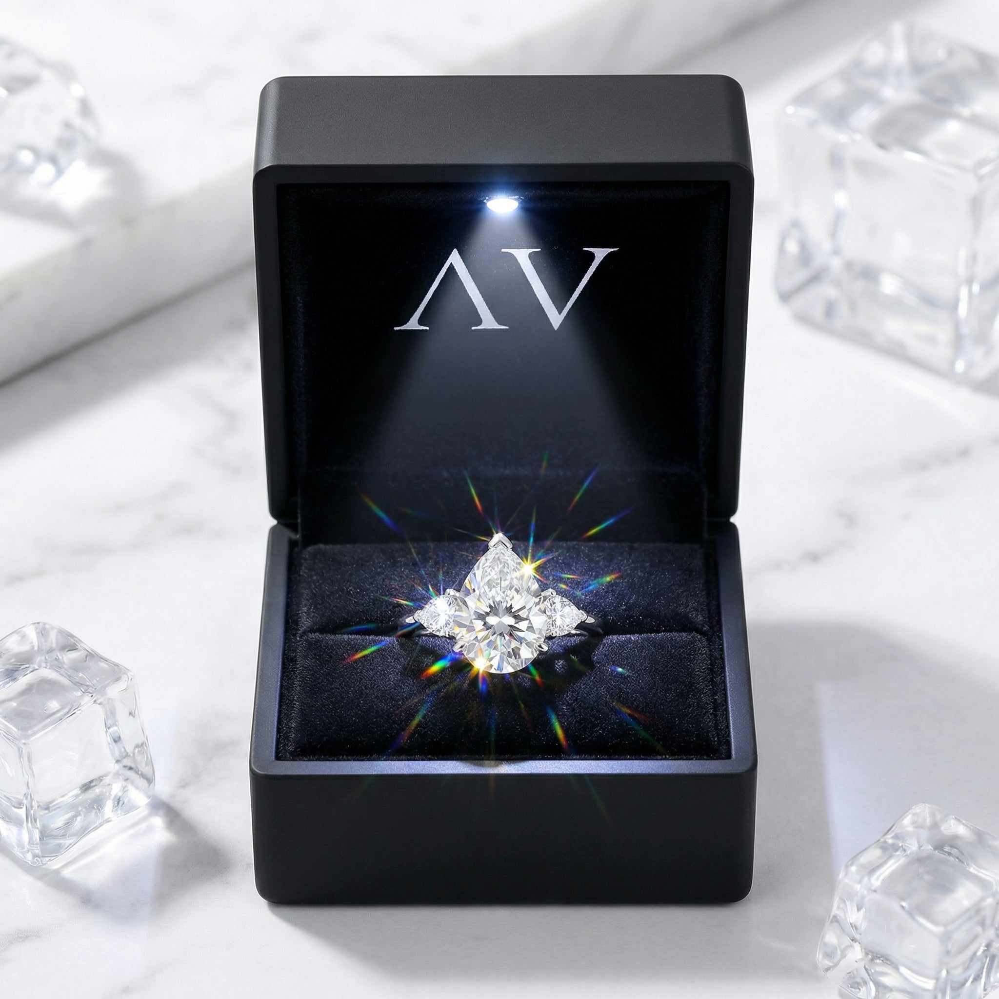 Pear cut simulated diamond trio ring in a black LED-lighted jewelry box on a marble surface.
