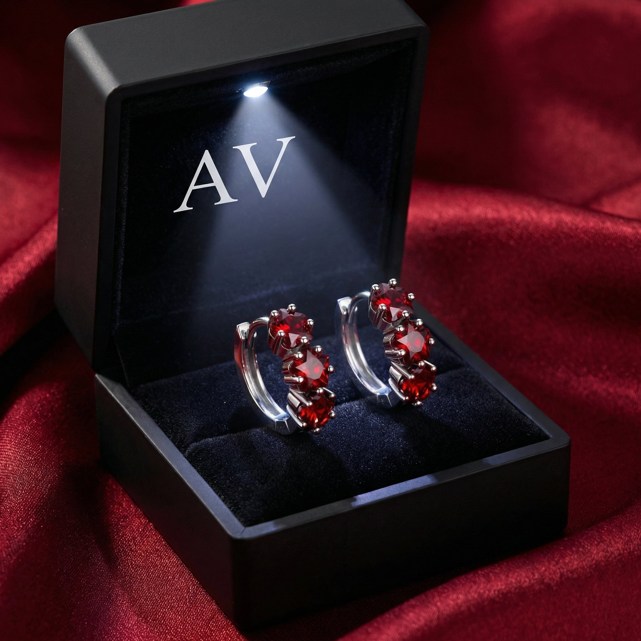 Star-cut simulated ruby huggie earrings inside a black LED-lit gift box on red fabric.