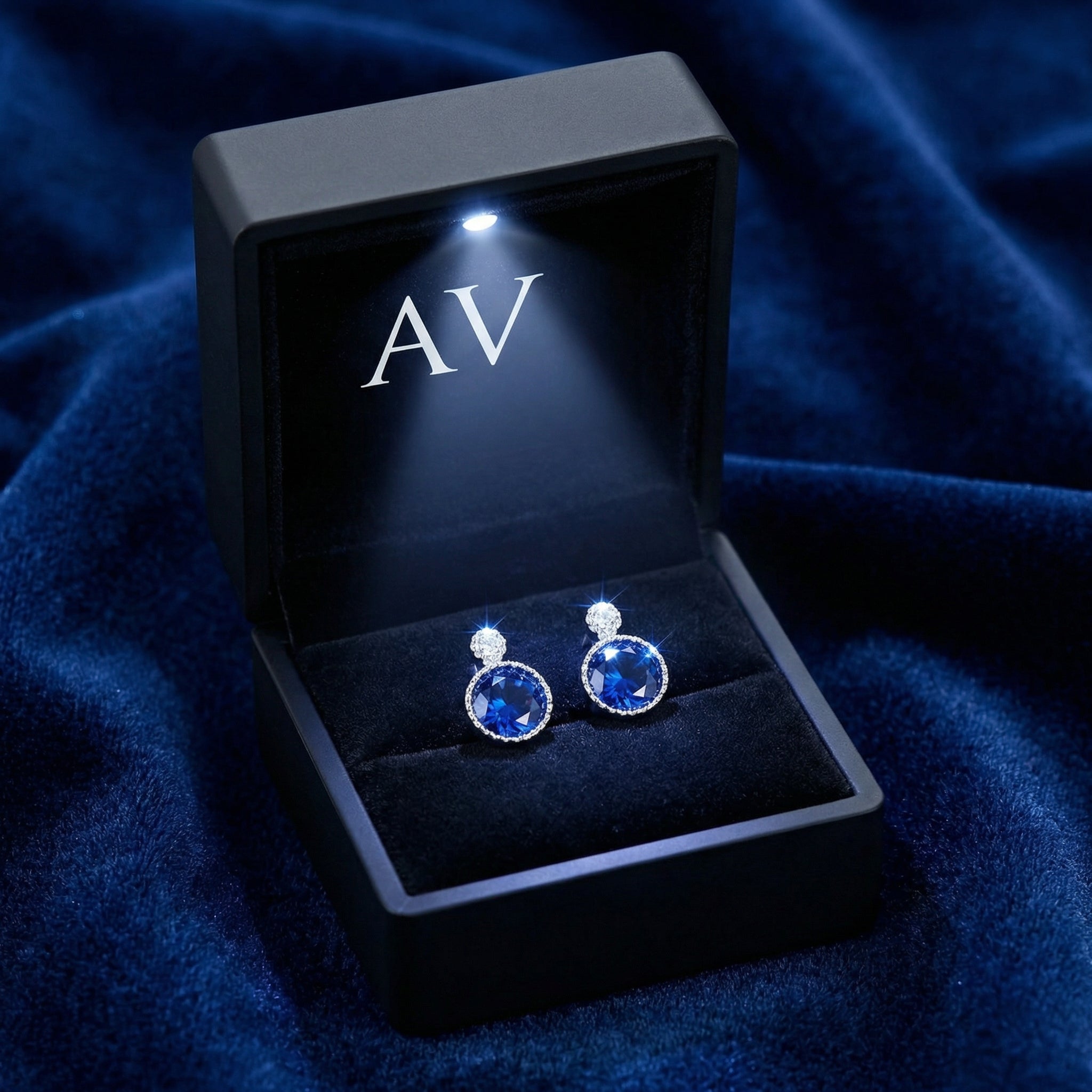 Pair of blue sapphire sterling silver stud earrings in a lighted black AV branded jewelry gift box.