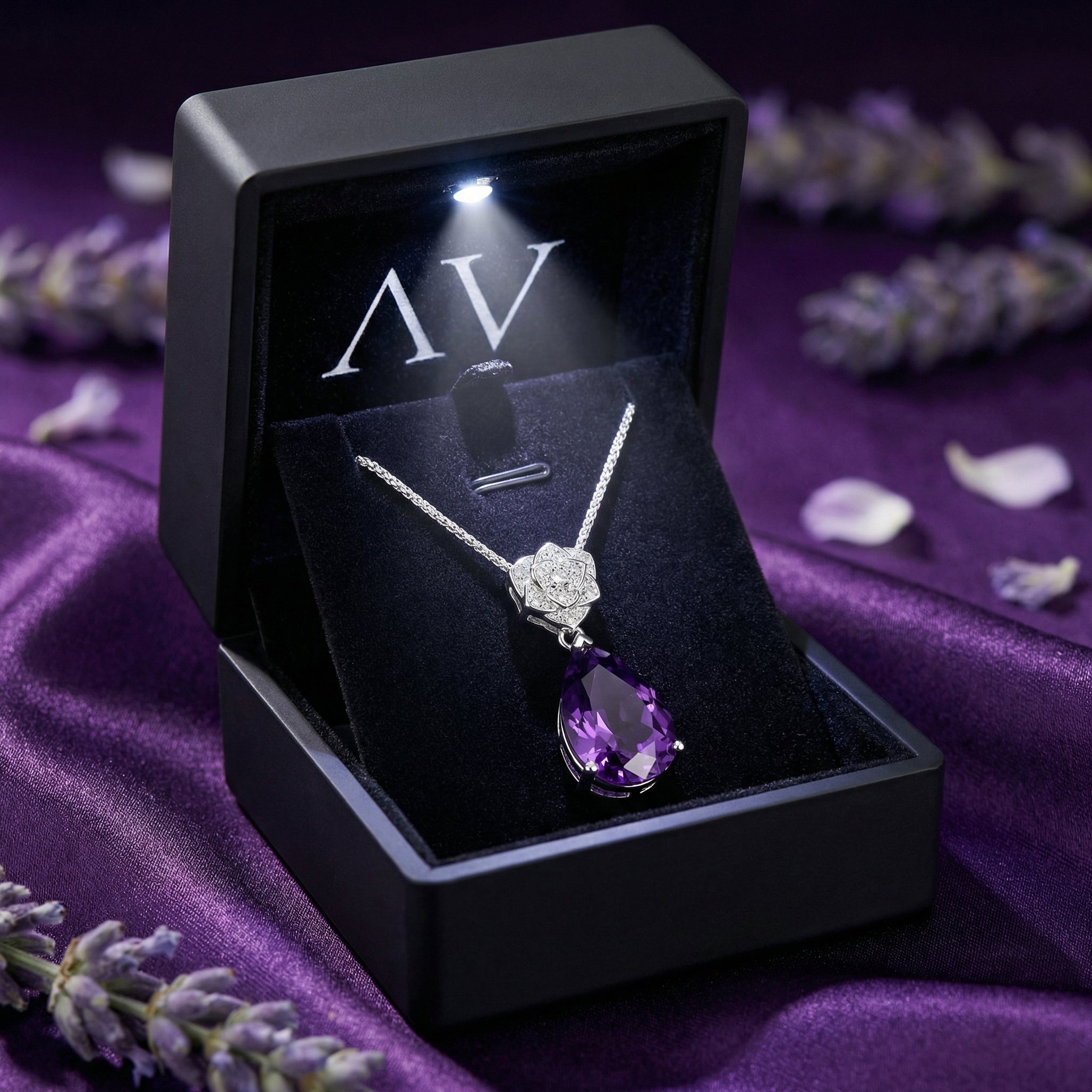 Pear-cut amethyst silver necklace in a lighted black jewelry presentation box on purple fabric.