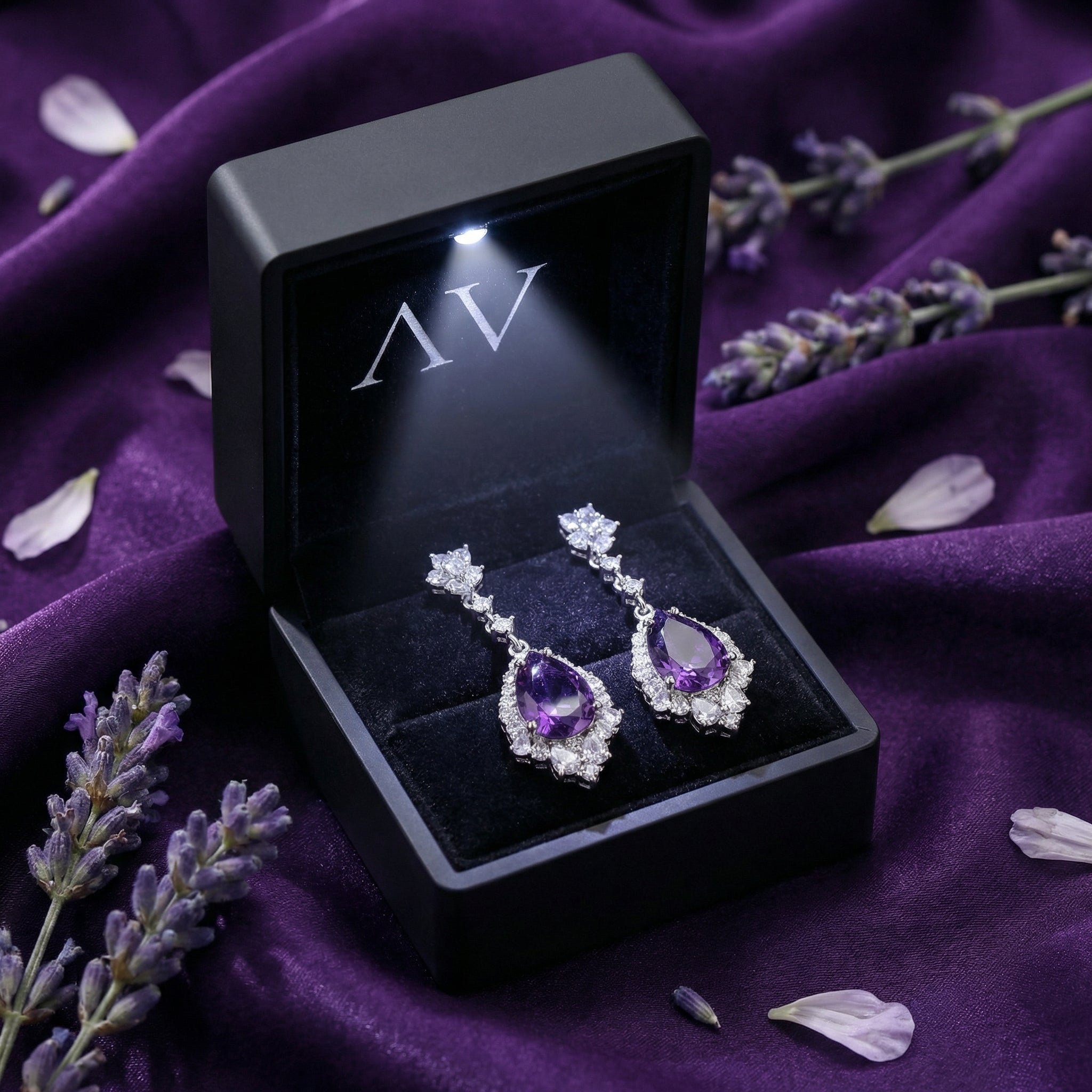 Pear cut natural amethyst drop earrings in a black LED-lit gift box on purple silk with lavender.