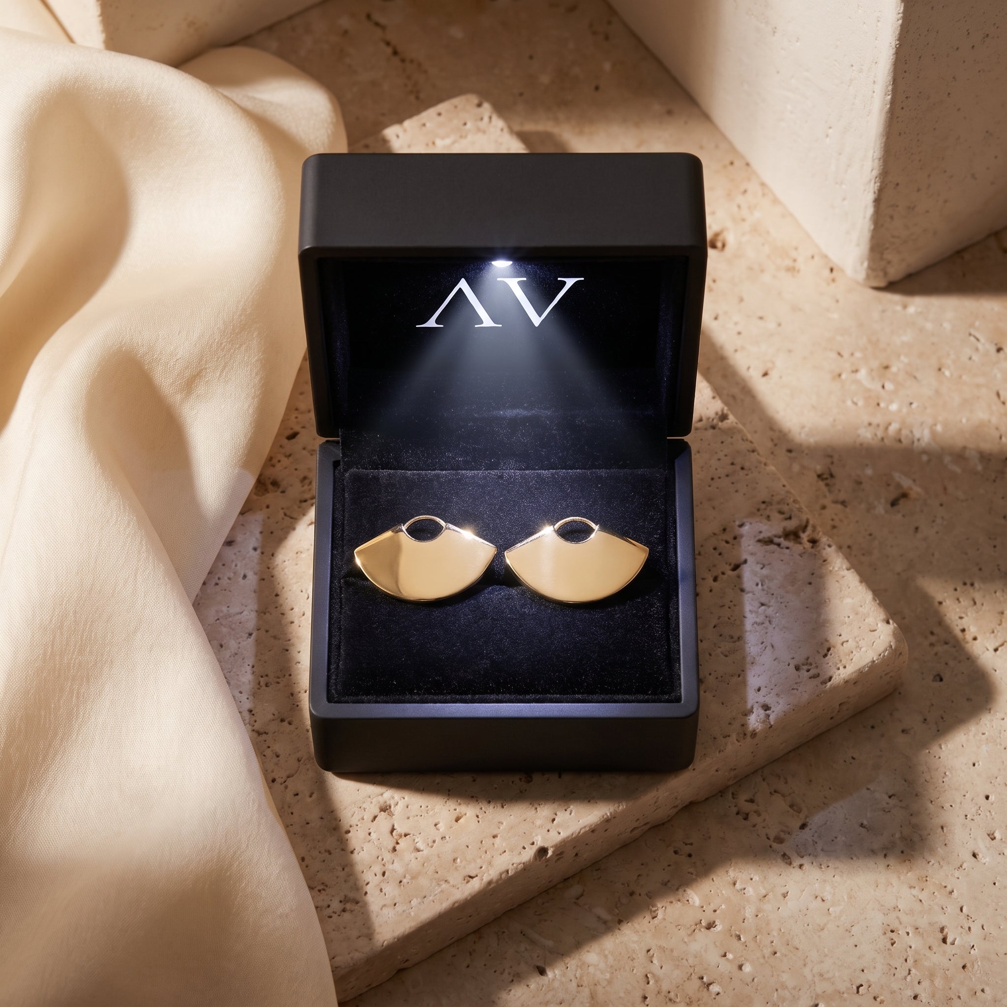 Gold fan earrings in 18K gold PVD stainless steel inside a lighted black gift box.