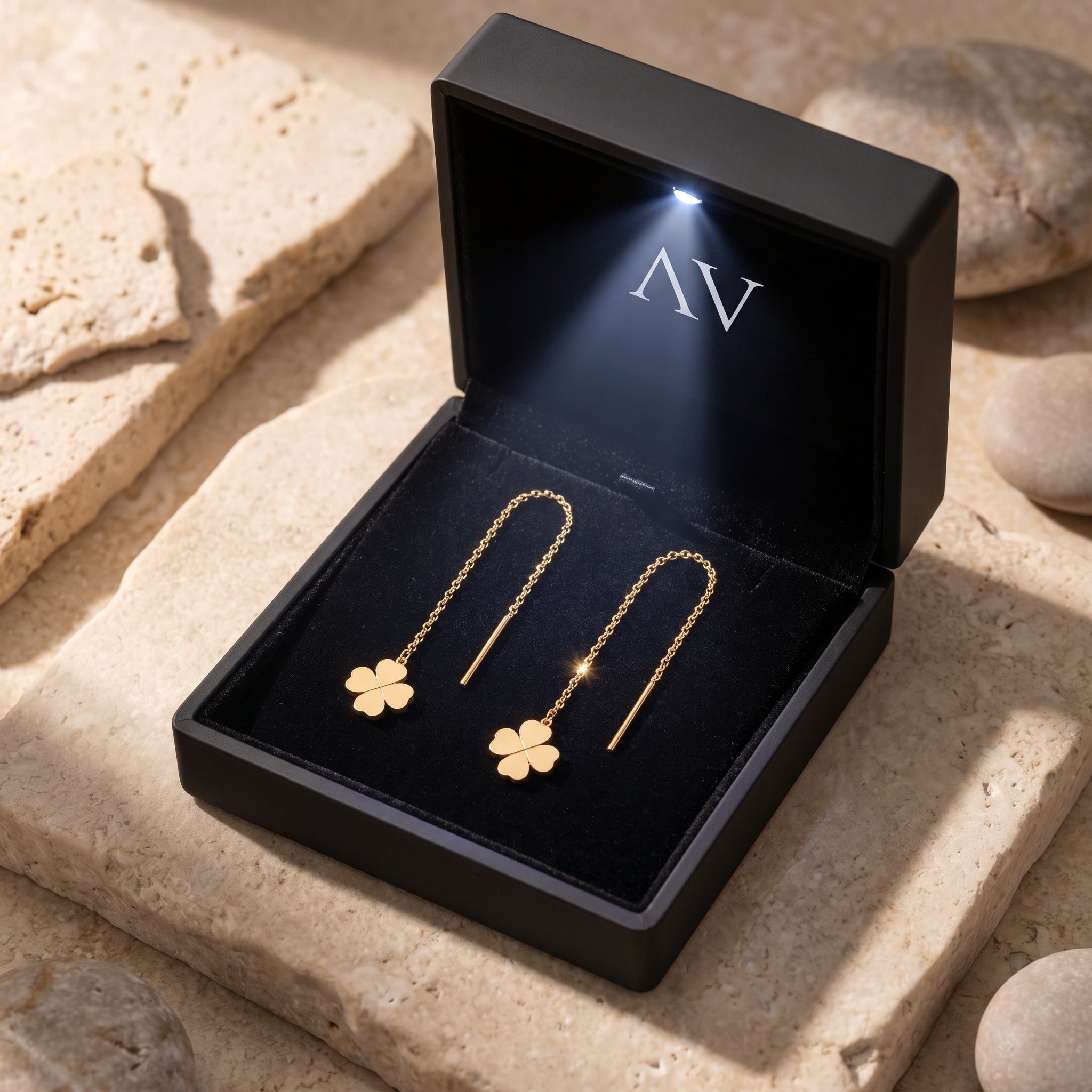 18K gold finish clover threader earrings in a premium black LED-lit gift box on a stone surface.