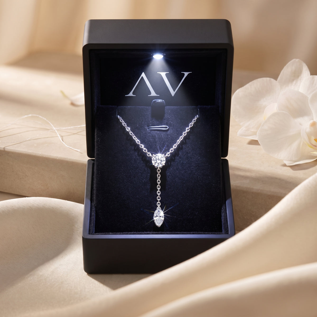 Silver moissanite lariat necklace presented in a black LED-lit gift box on a silk background.