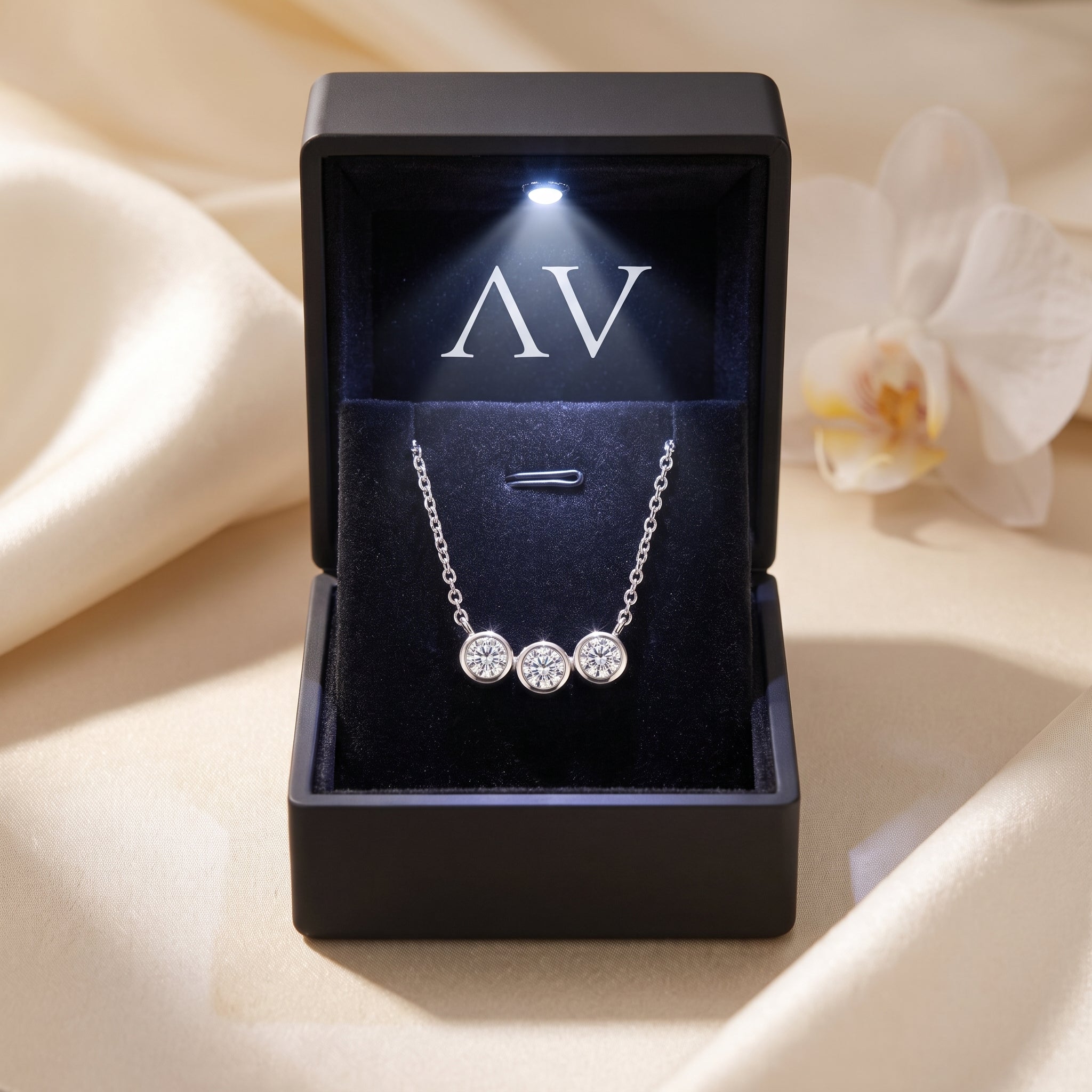 Silver three-stone moissanite pendant necklace presented in a black LED-lit gift box.