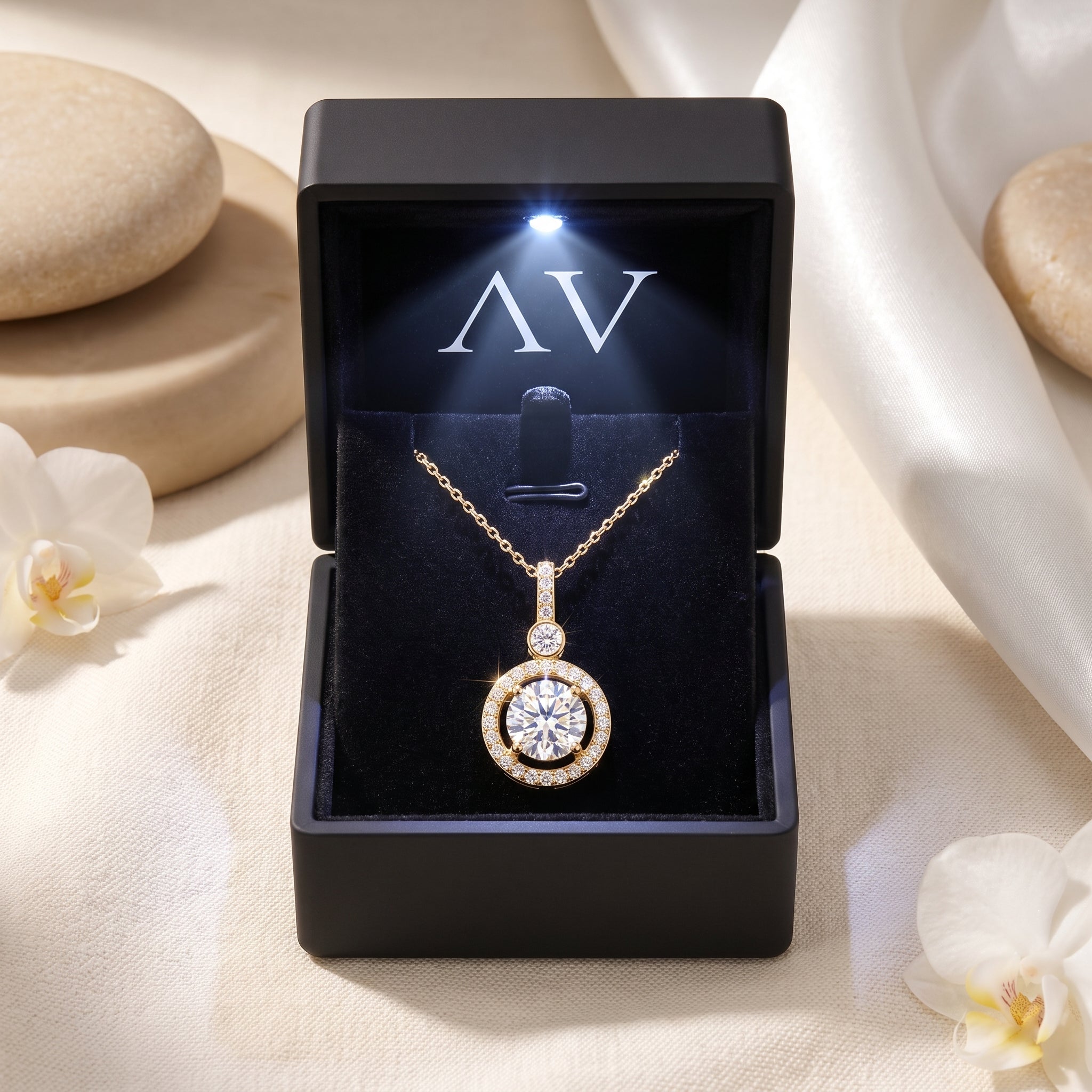 The Antoinette moissanite halo necklace in solid gold, displayed in a black LED-lit gift box with the AV logo and white flowers.