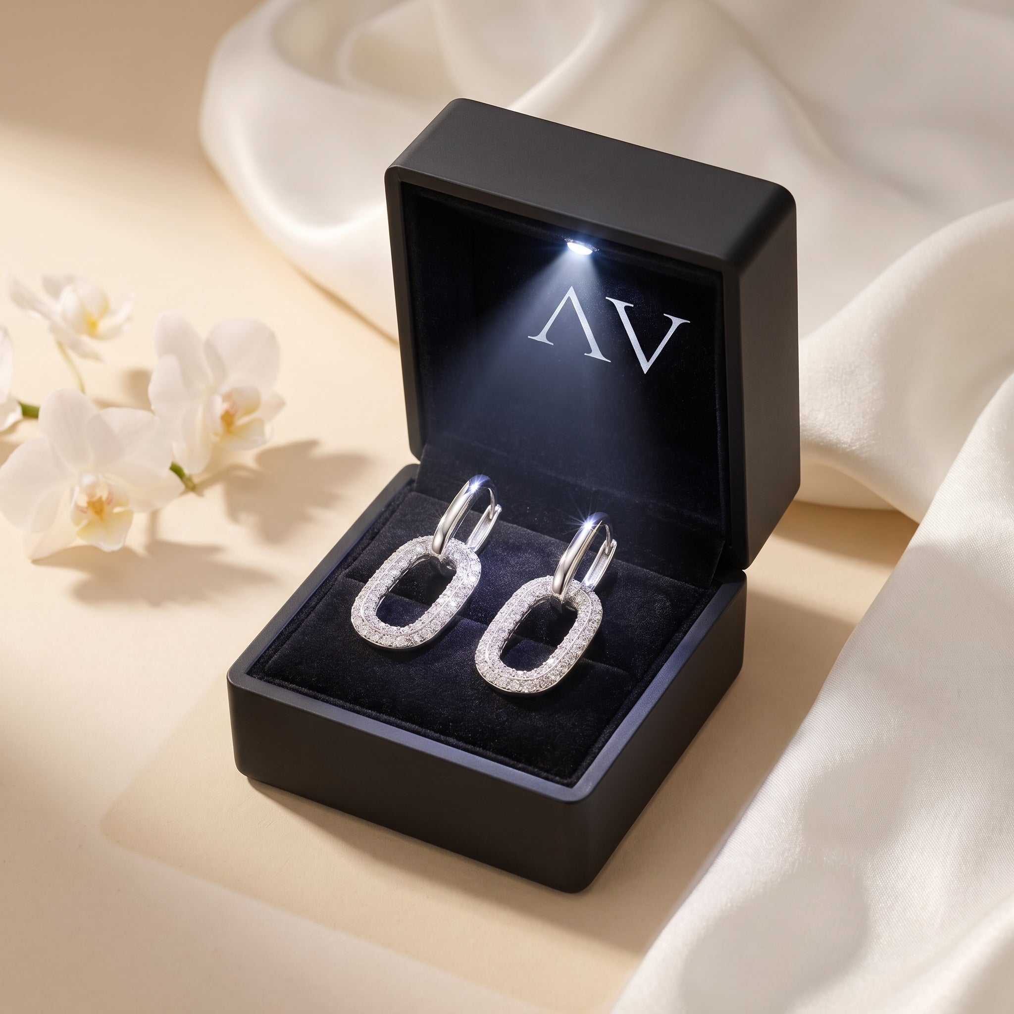 Silver moissanite drop earrings in a black LED-lit gift box.