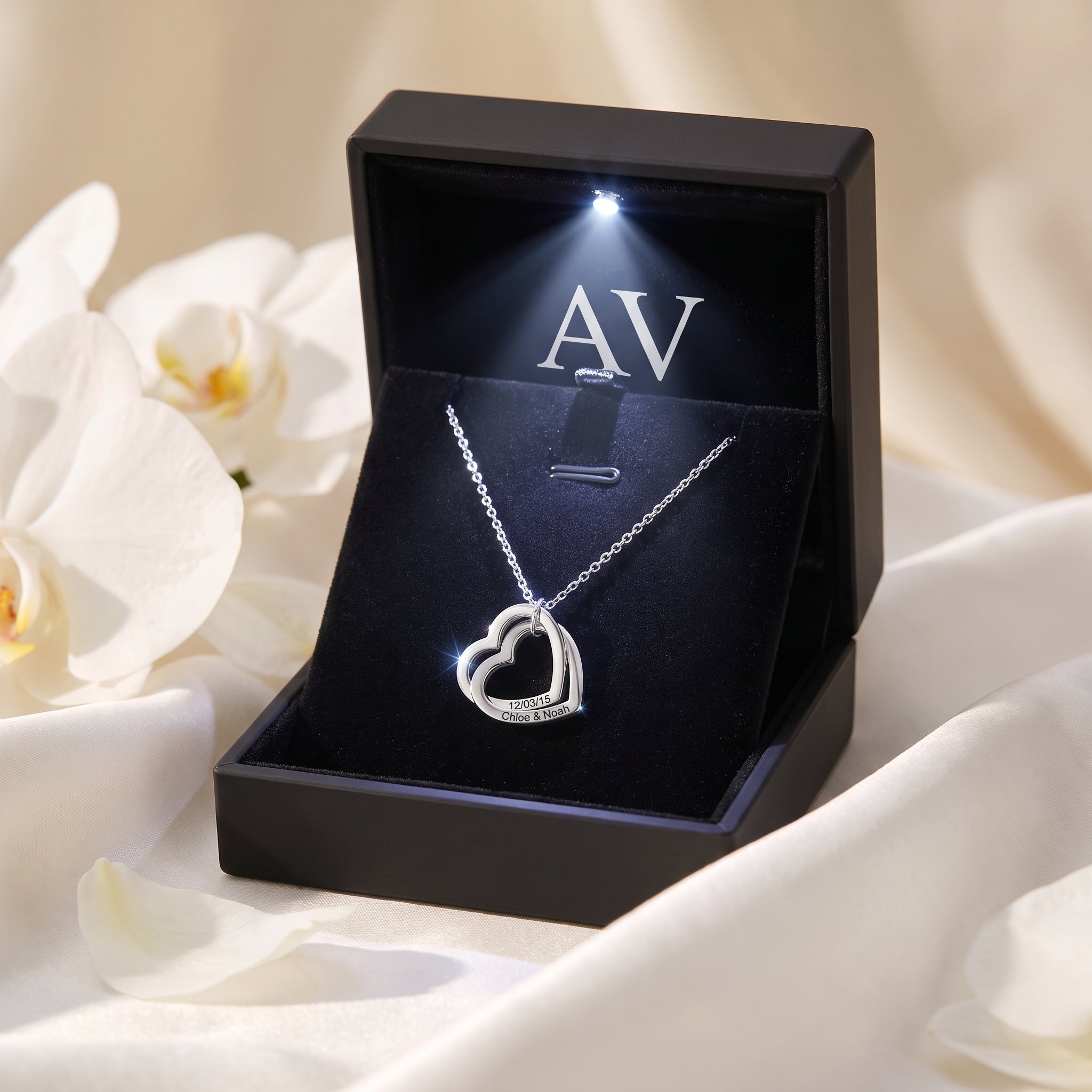 Silver interlocking heart necklace inside a premium black LED-lit gift box with white petals.
