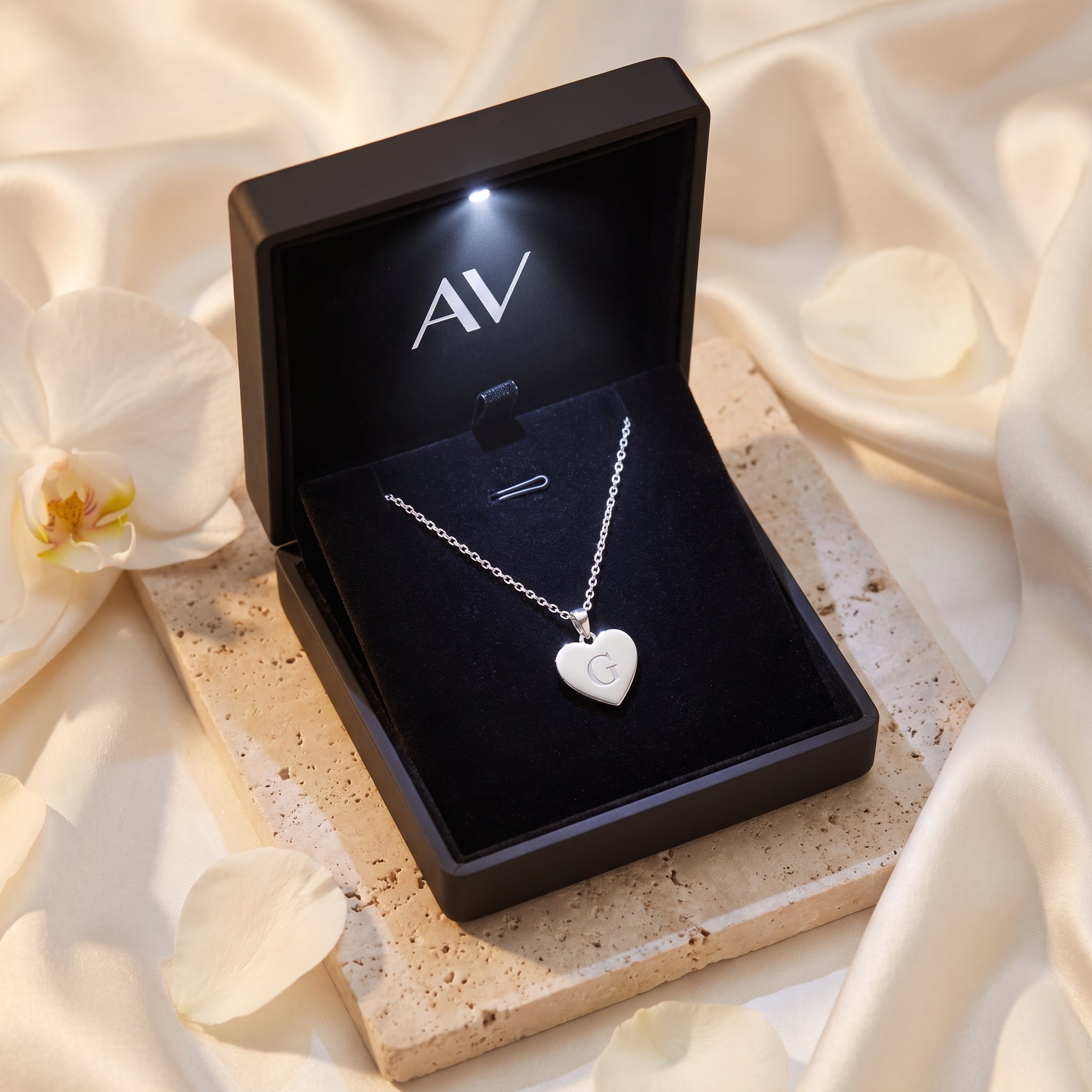Silver heart pendant necklace with engraved 'G' inside a black LED-lit jewelry gift box.