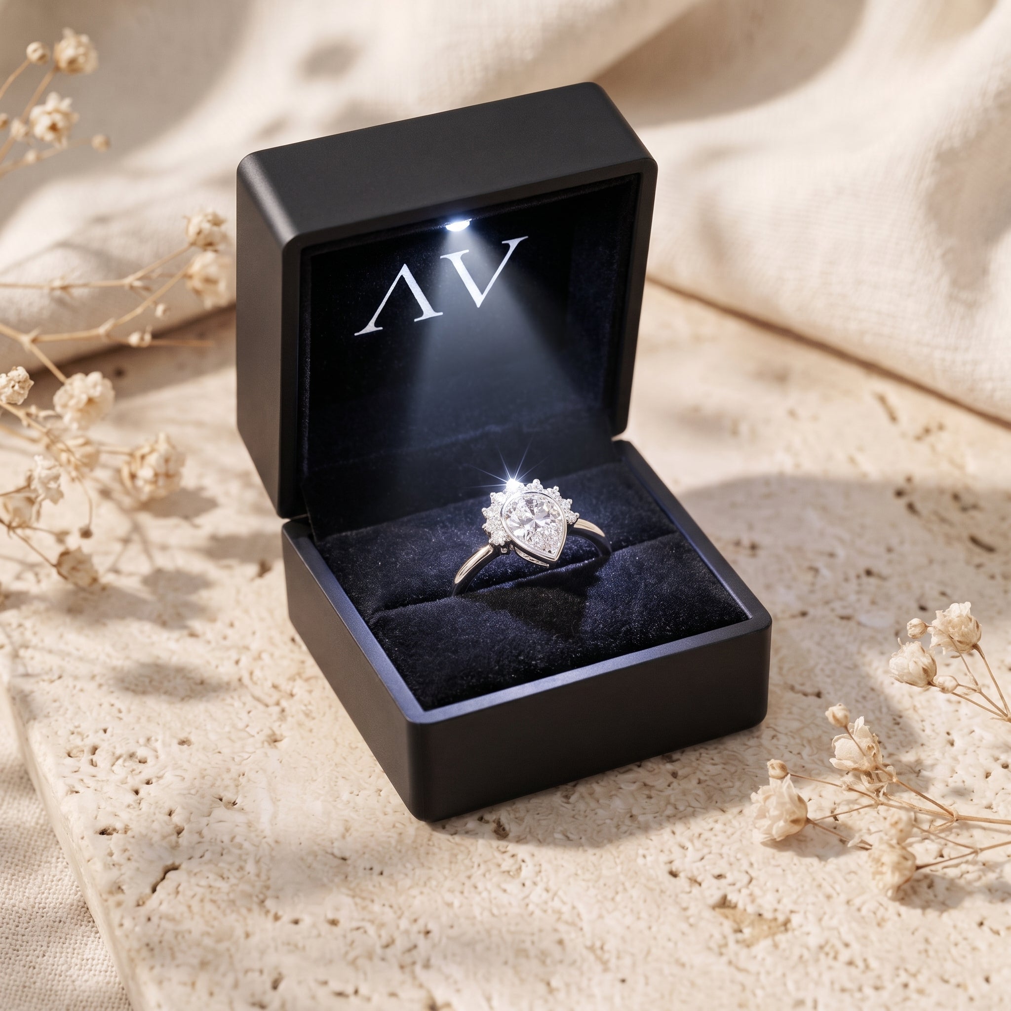 Silver pear-cut moissanite ring inside a lighted black jewelry presentation box.