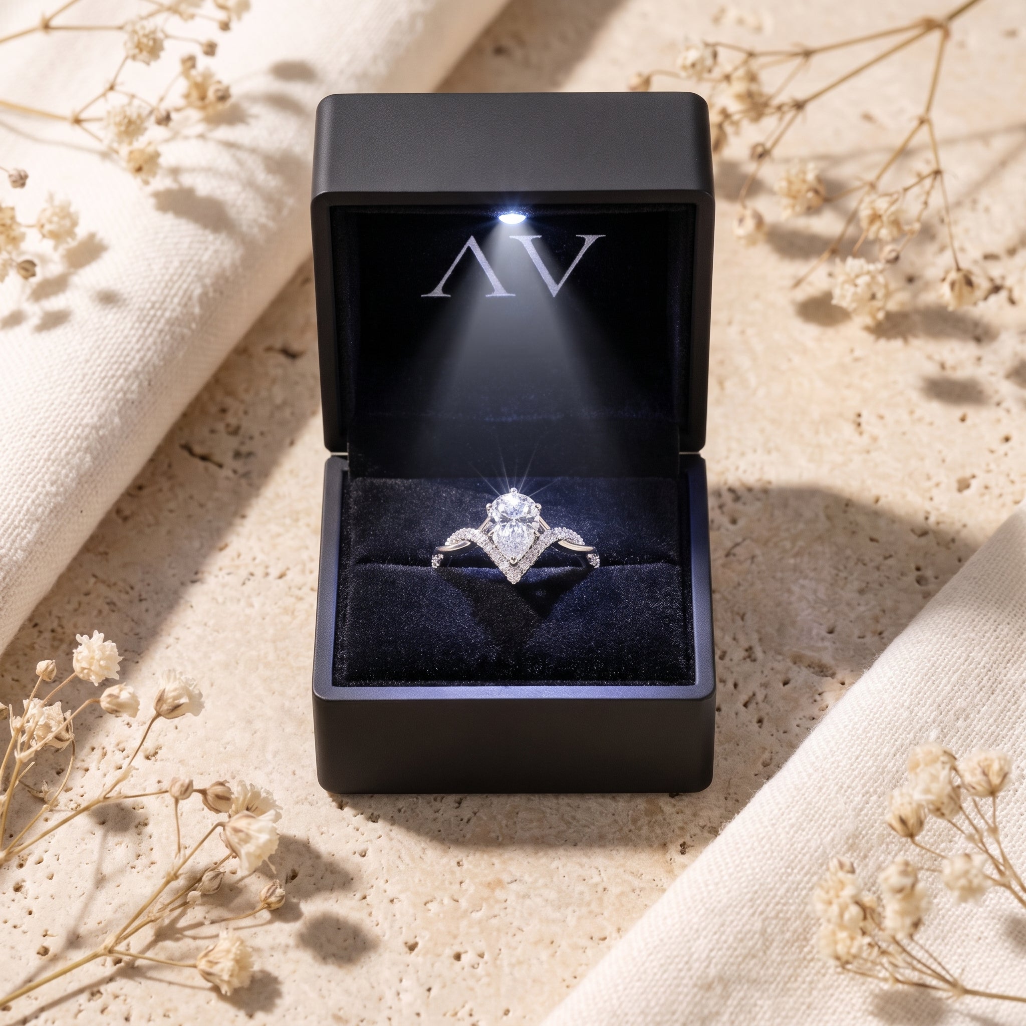 Silver pear-cut moissanite ring displayed in a black LED-lit jewelry presentation box.