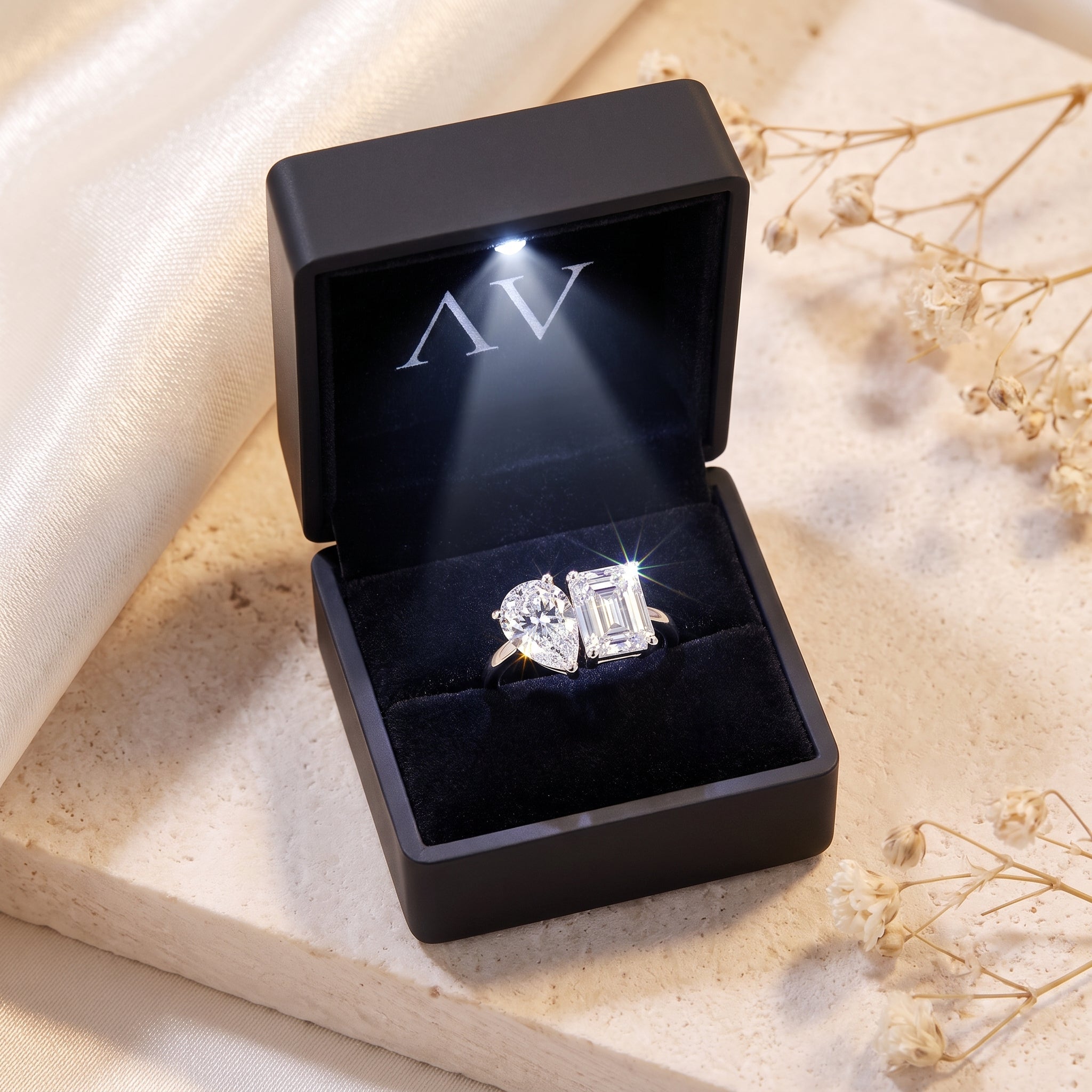 Silver bypass ring with pear and emerald cut simulated diamonds in a black LED-lit jewelry presentation box.