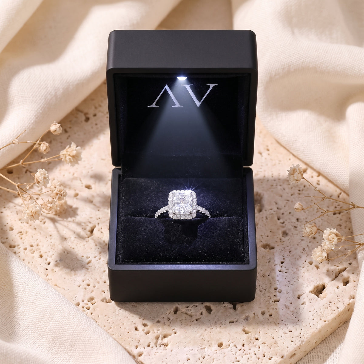 Radiant-cut cubic zirconia halo silver ring inside a black lighted presentation box on a styled background.