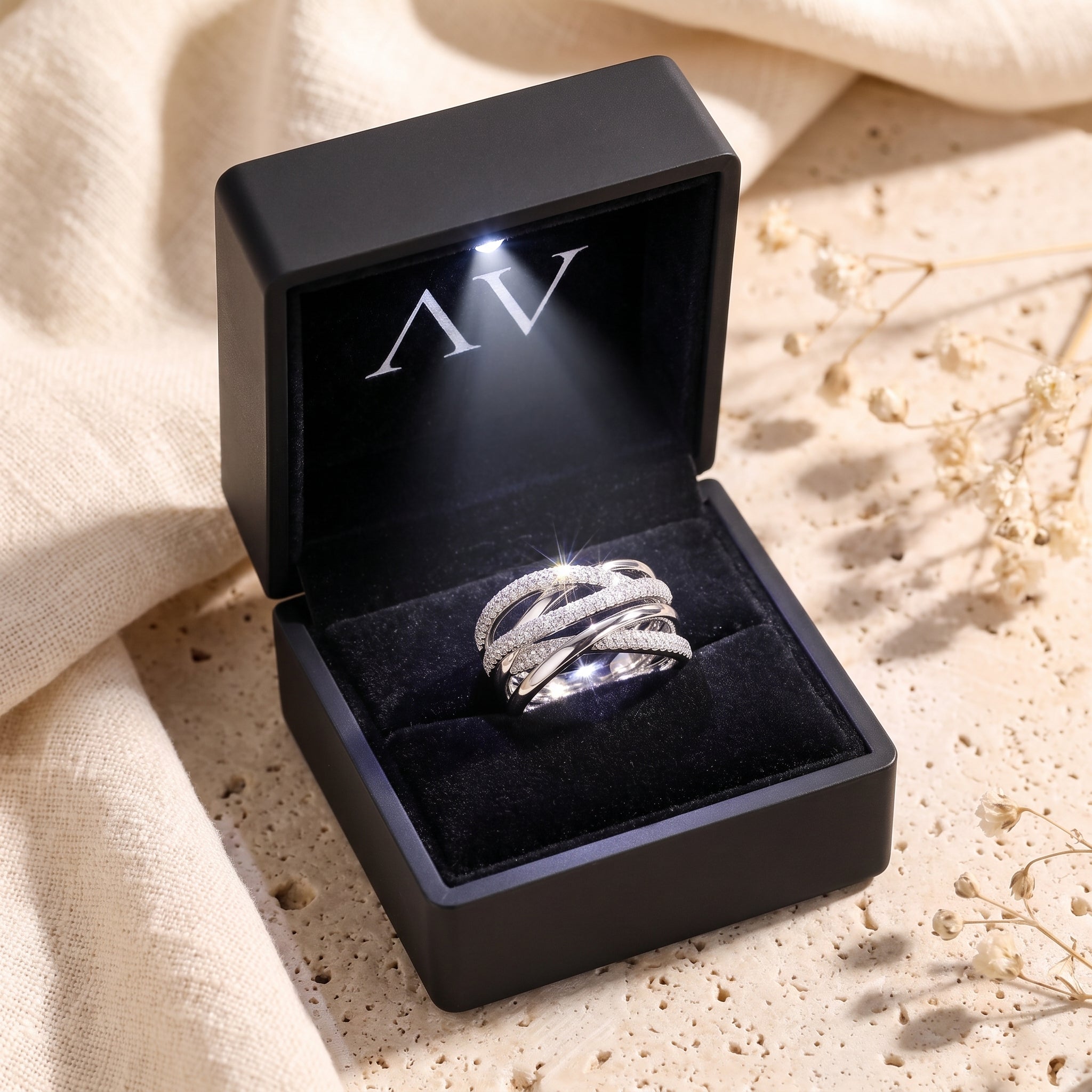Silver crossover ring with simulated diamonds in a lighted black gift box.