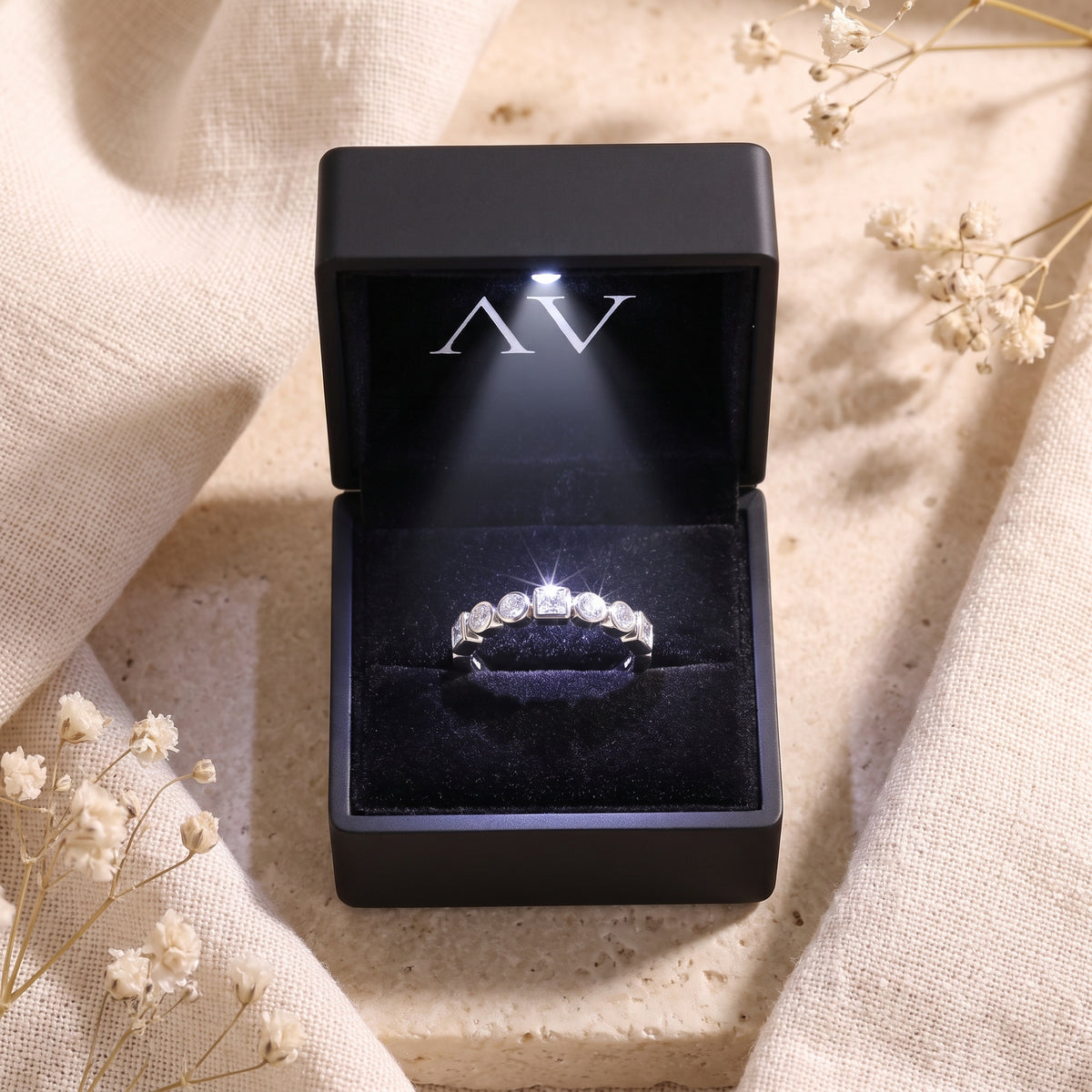 Silver eternity band displayed in a black LED-lit jewelry box with floral accents.