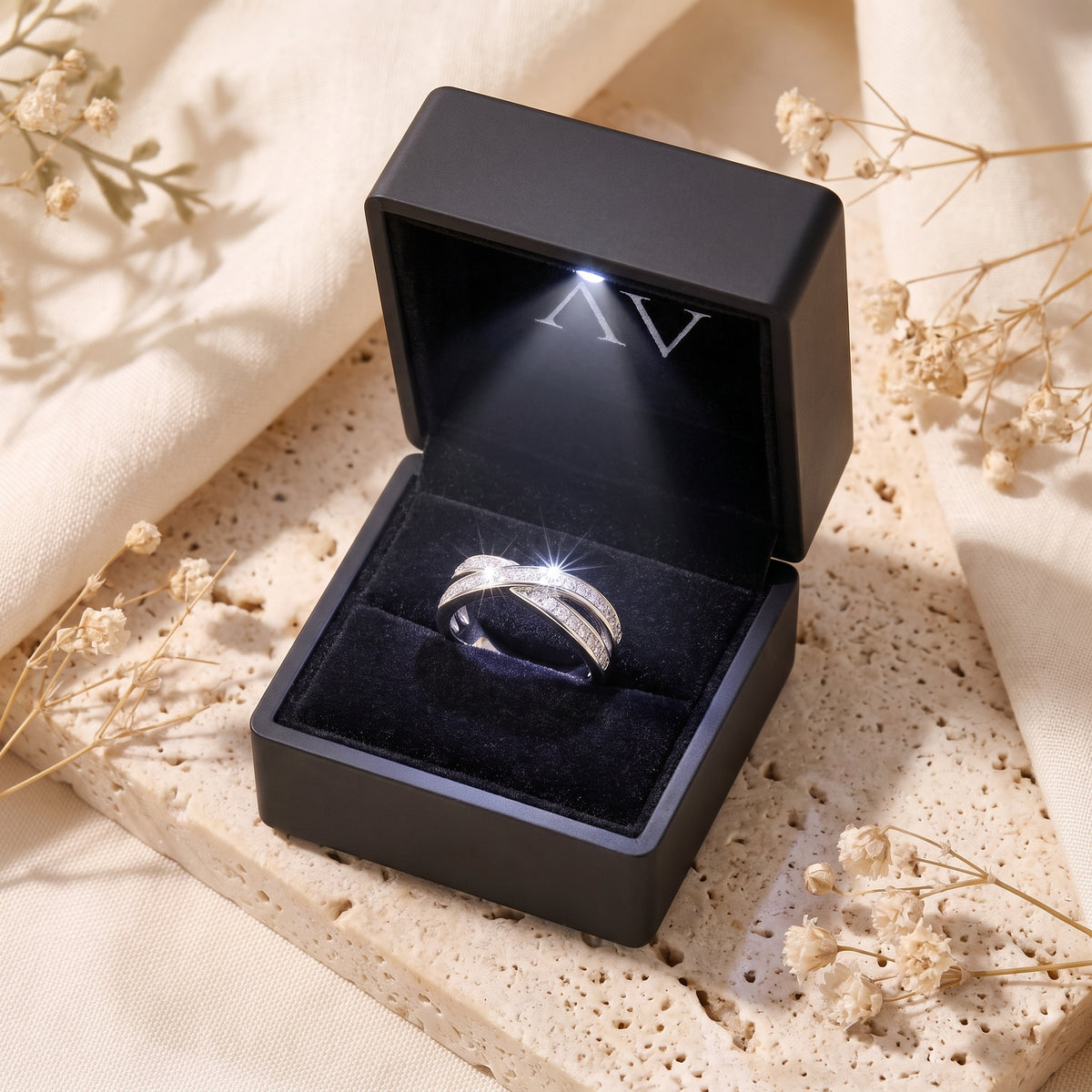 Silver crossover promise ring with round simulated diamonds in a black LED-lit box.