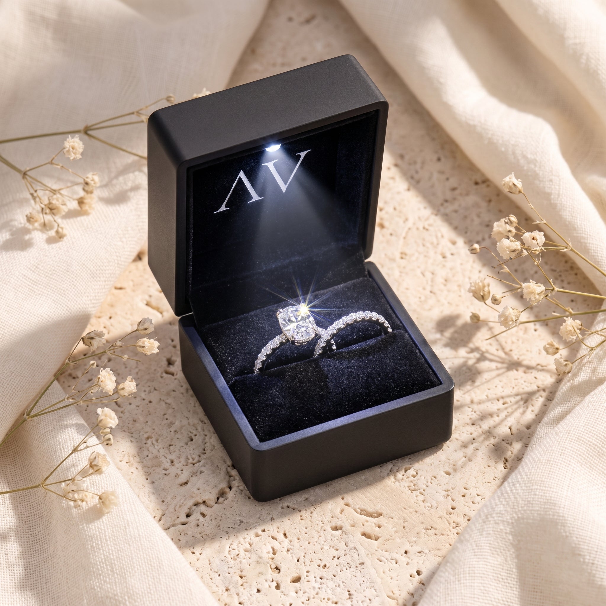 Silver oval-cut ring set inside a lighted black jewelry box on a styled surface.