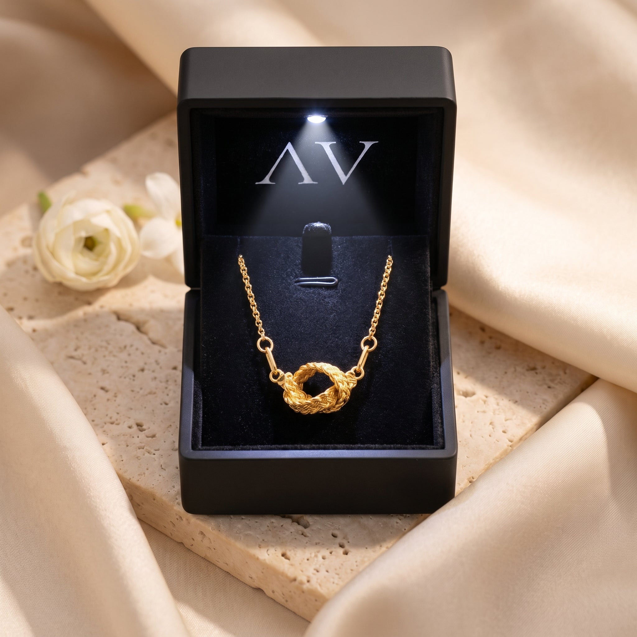 Gold knot necklace in a black LED-lit branded jewelry box.