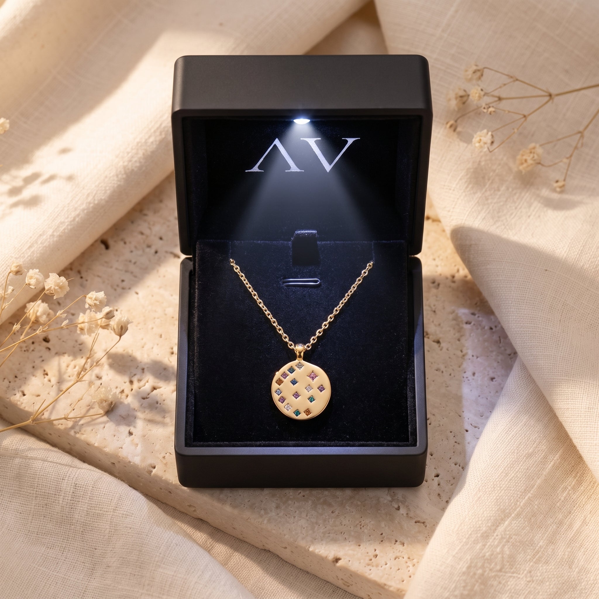 18K gold Astraline pendant necklace displayed in a black LED-lit jewelry gift box on a stone surface.