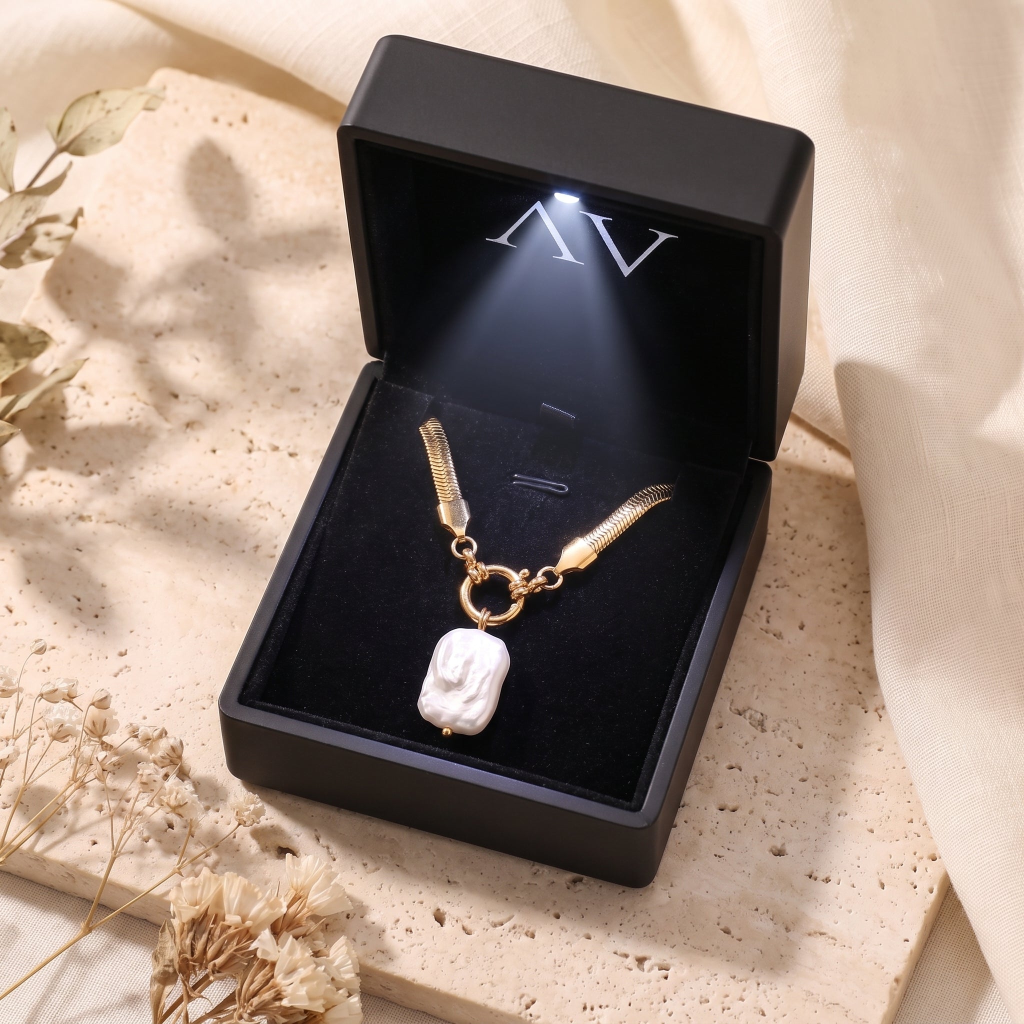 Gold herringbone necklace with a white baroque pearl pendant inside a black LED-lit jewelry gift box.