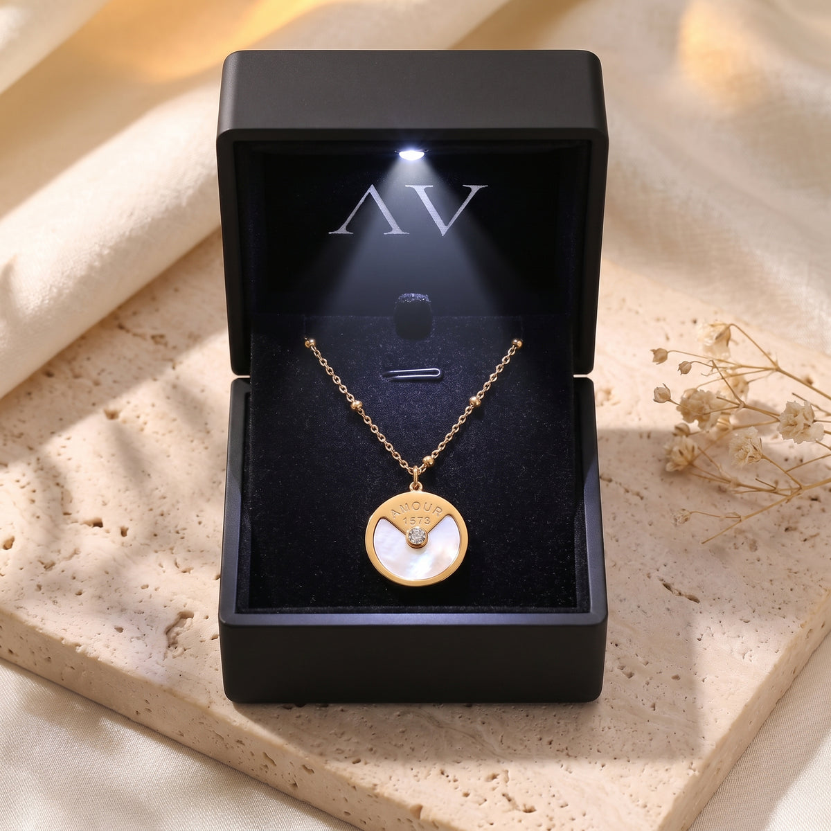 Gold pendant necklace inside a black LED-lit jewelry box on a stone surface.