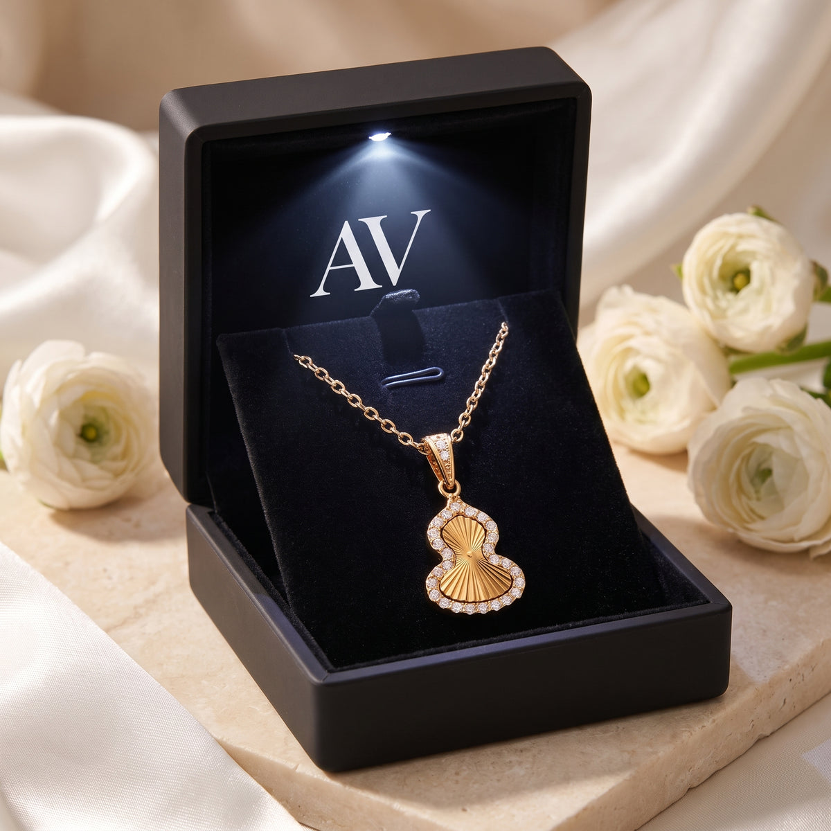 Gold gourd pendant necklace with cubic zirconia halo inside a lighted black jewelry box.